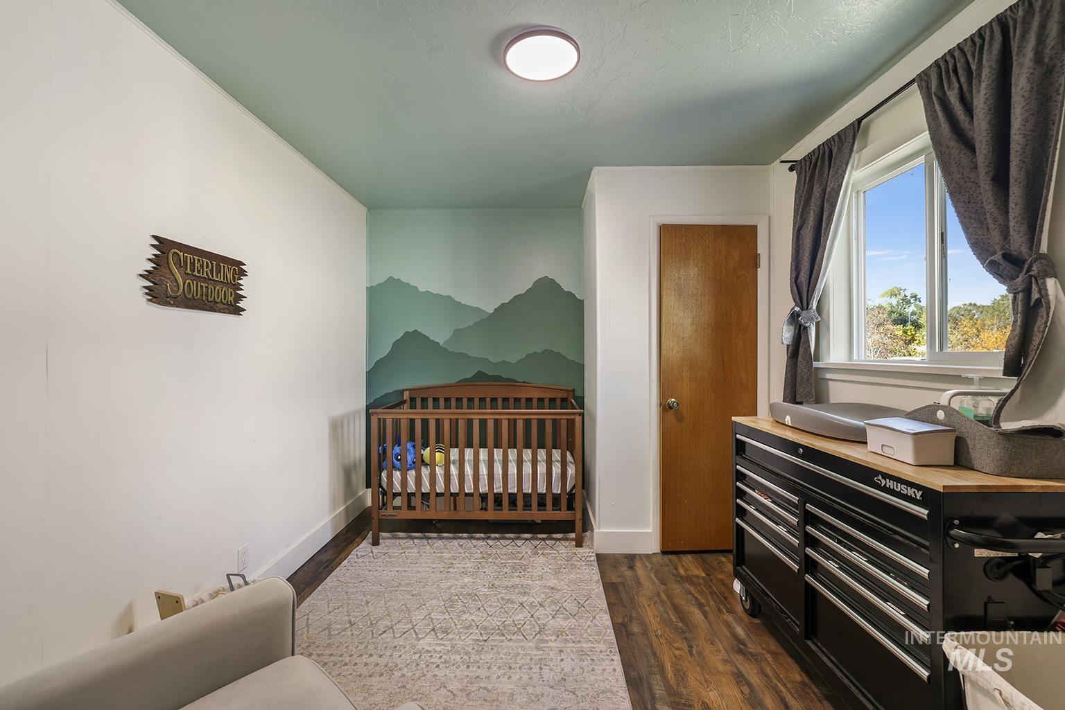 Bedroom with a crib and dark wood-type flooring
