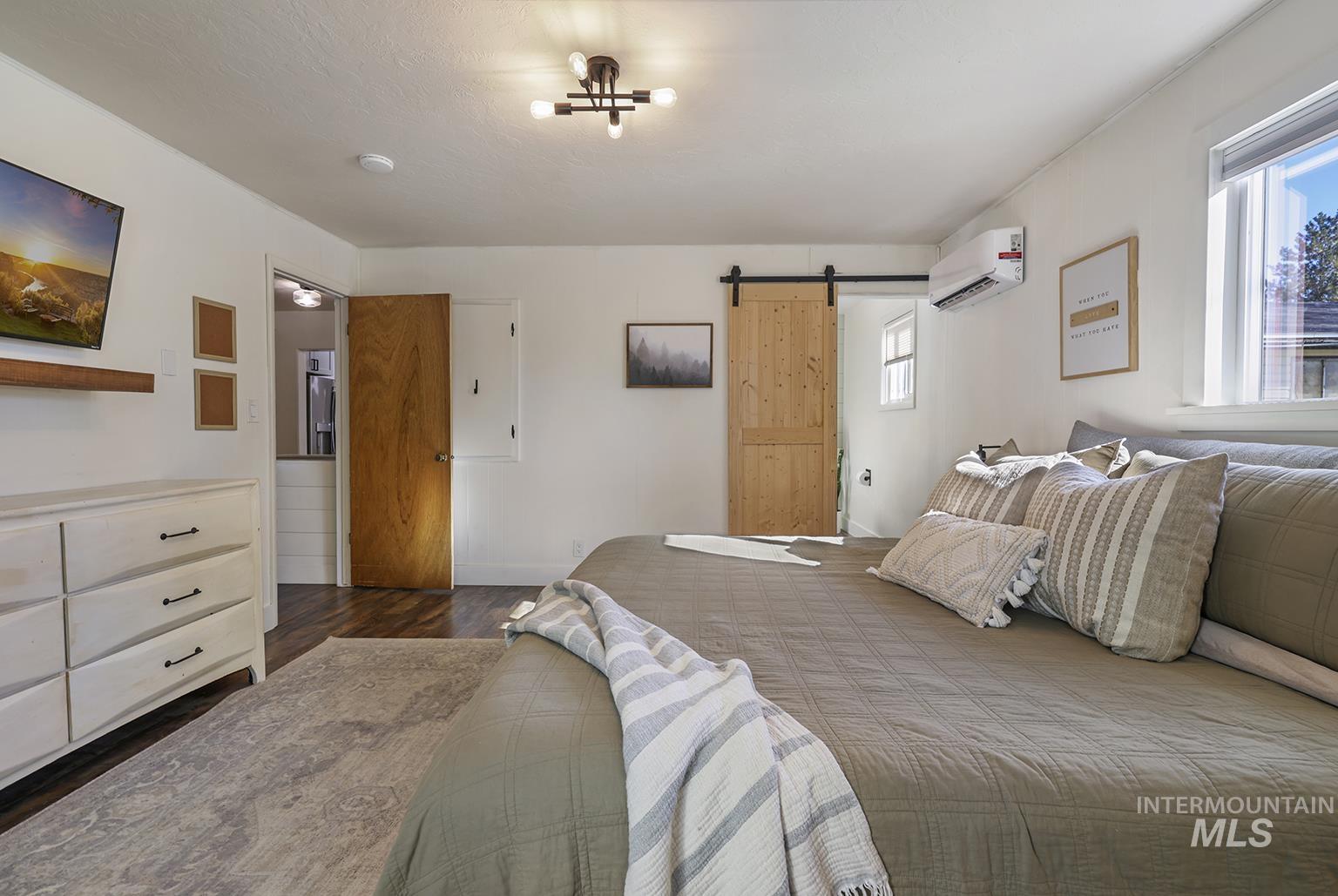 Bedroom with a barn door, dark wood-style flooring, and a wall unit AC