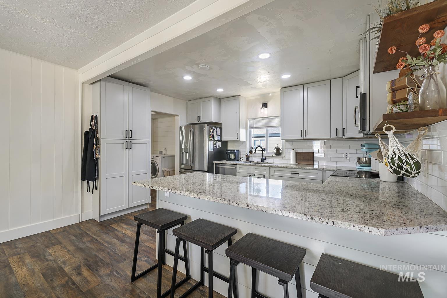 Kitchen with a breakfast bar area, light stone counters, a peninsula, white cabinets, and recessed lighting