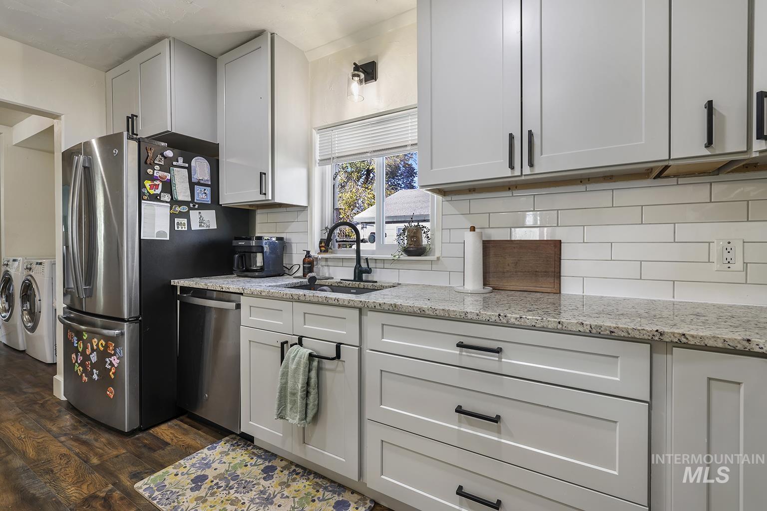 Kitchen with separate washer and dryer, stainless steel appliances, dark wood-style floors, light stone counters, and tasteful backsplash