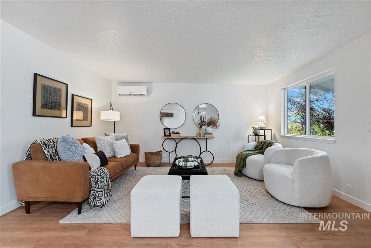 Living area featuring light wood-type flooring, a textured ceiling, and a wall mounted air conditioner