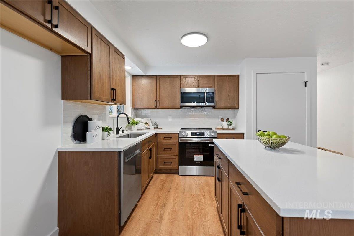 Kitchen featuring brown cabinets, appliances with stainless steel finishes, light wood-style floors, and backsplash