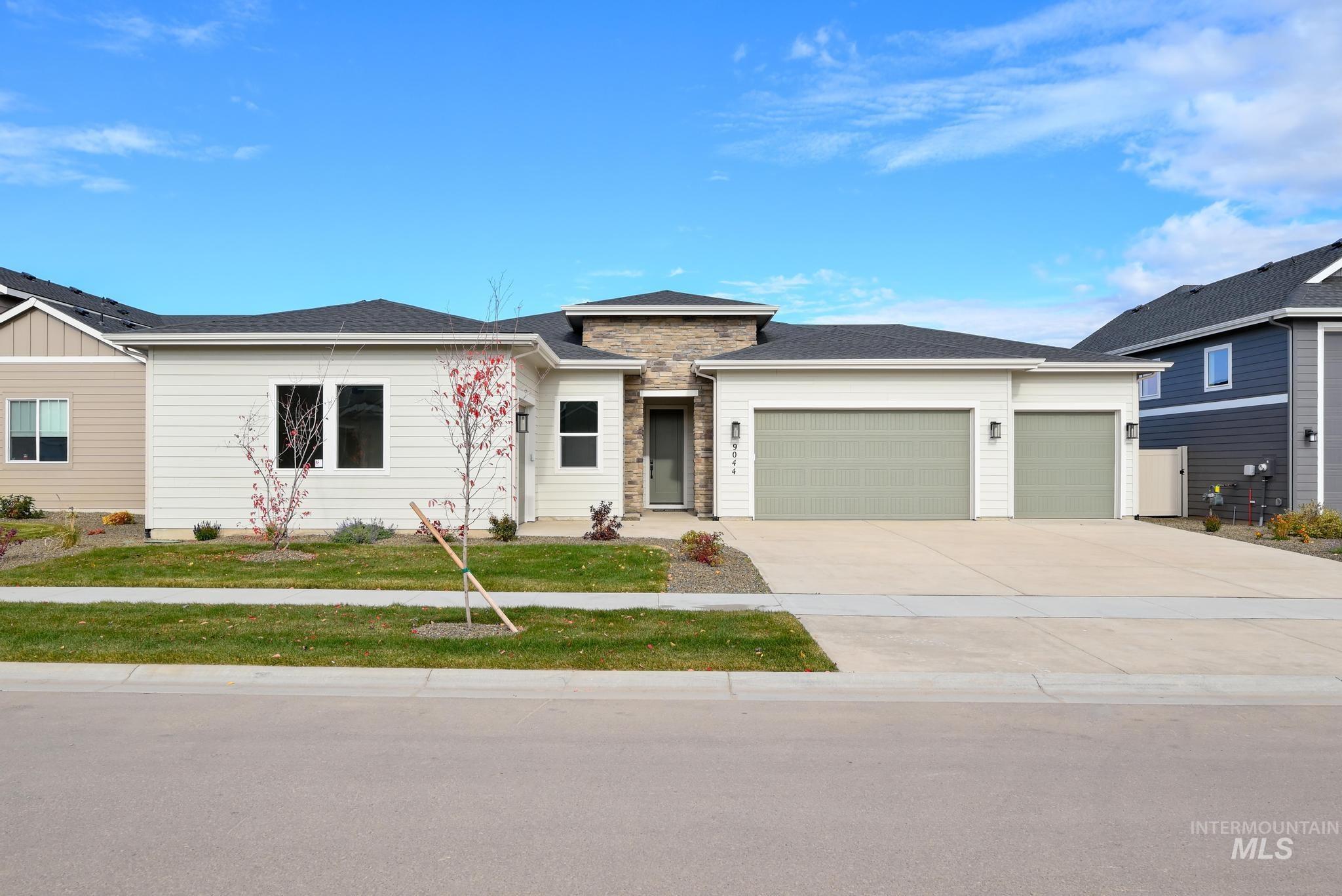 View of front of property featuring a garage, driveway, a front lawn, and stone siding