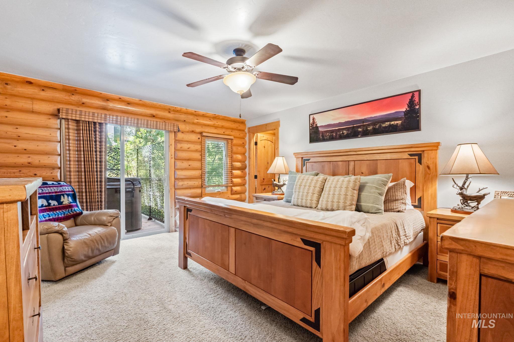 Bedroom featuring access to exterior, light colored carpet, ceiling fan, and rustic walls