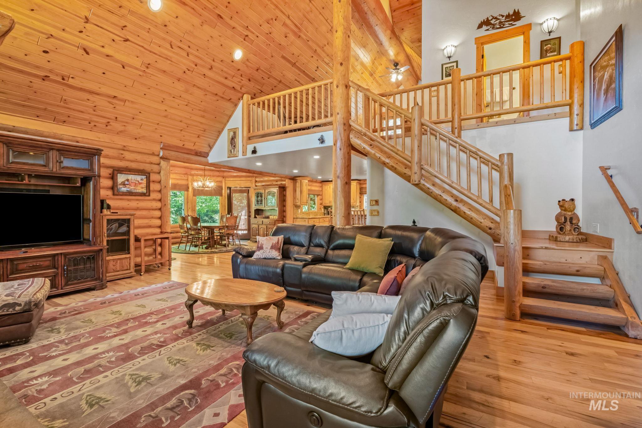 Living area featuring high vaulted ceiling, log walls, hardwood / wood-style floors, stairs, and recessed lighting
