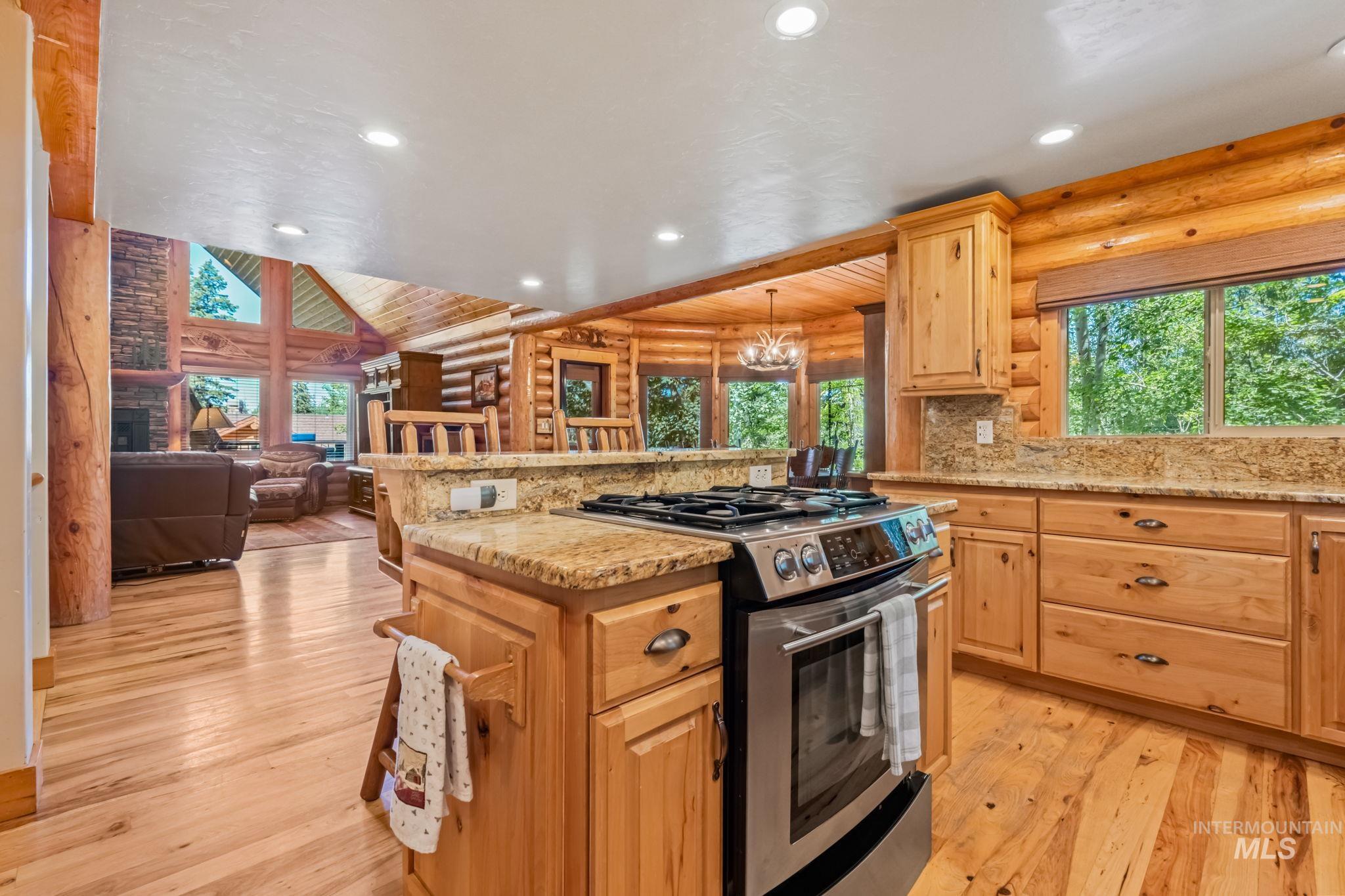 Kitchen featuring log walls, light stone counters, stainless steel range with gas stovetop, recessed lighting, and plenty of natural light