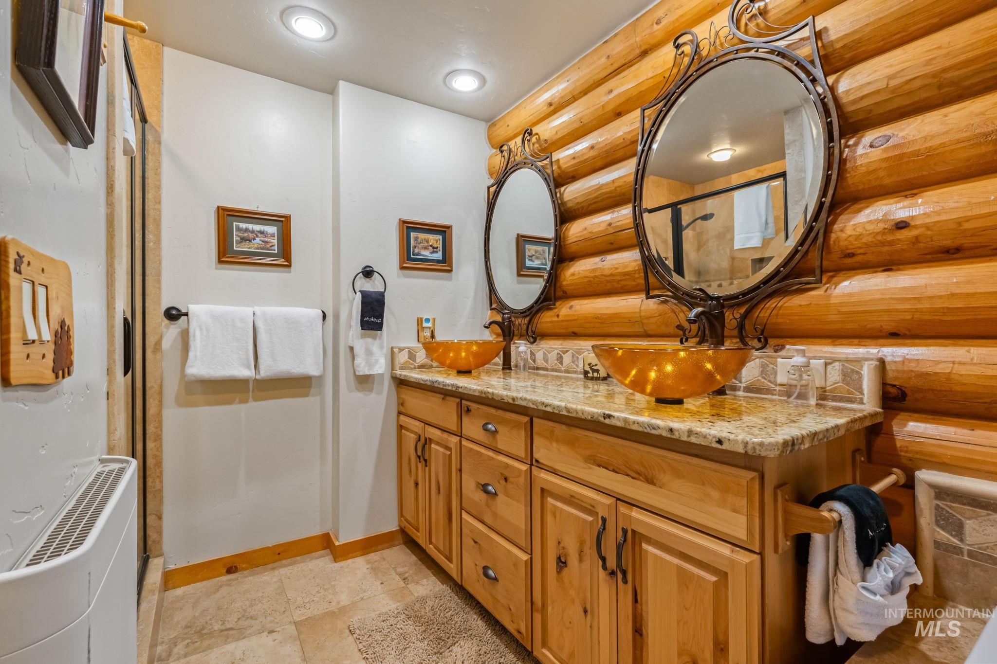 Bathroom featuring double vanity, log walls, stone tile flooring, an enclosed shower, and recessed lighting