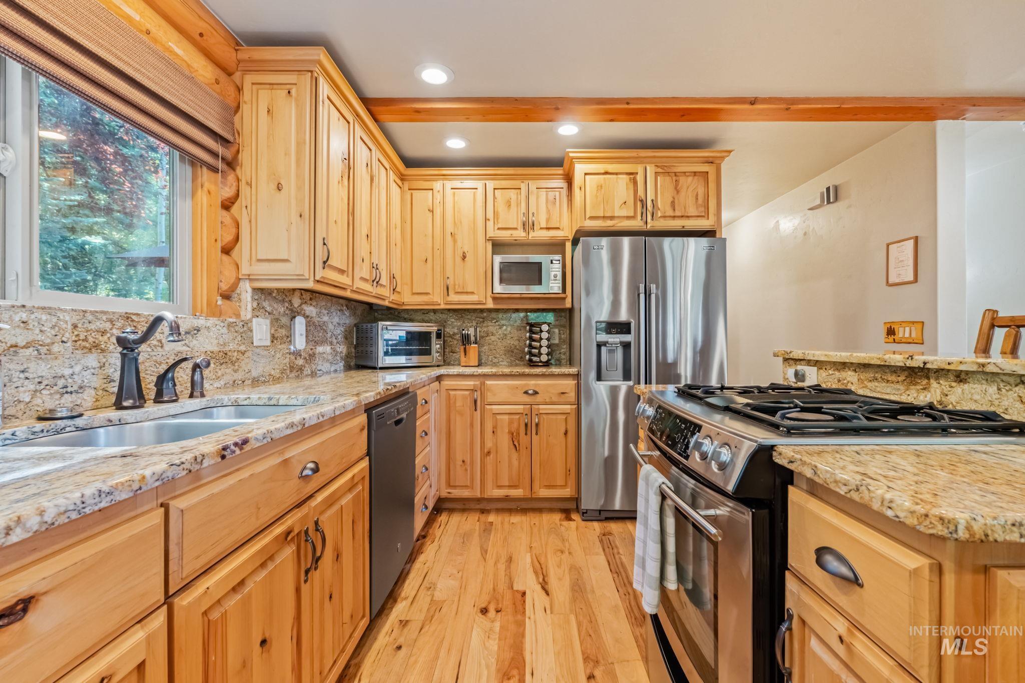 Kitchen with appliances with stainless steel finishes, light wood-style flooring, light stone counters, backsplash, and recessed lighting