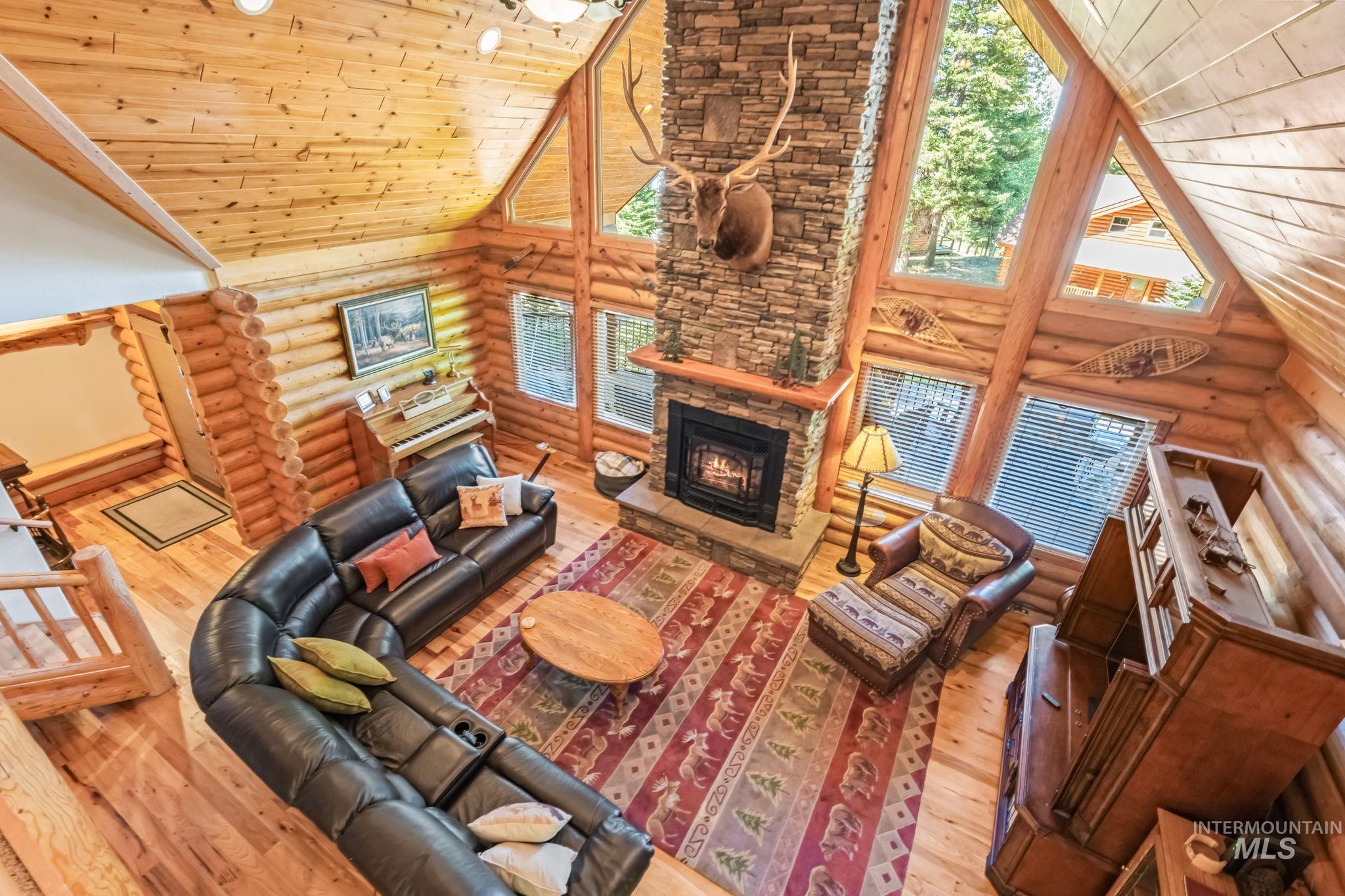 Living area with high vaulted ceiling, wood ceiling, hardwood / wood-style flooring, a stone fireplace, and log walls