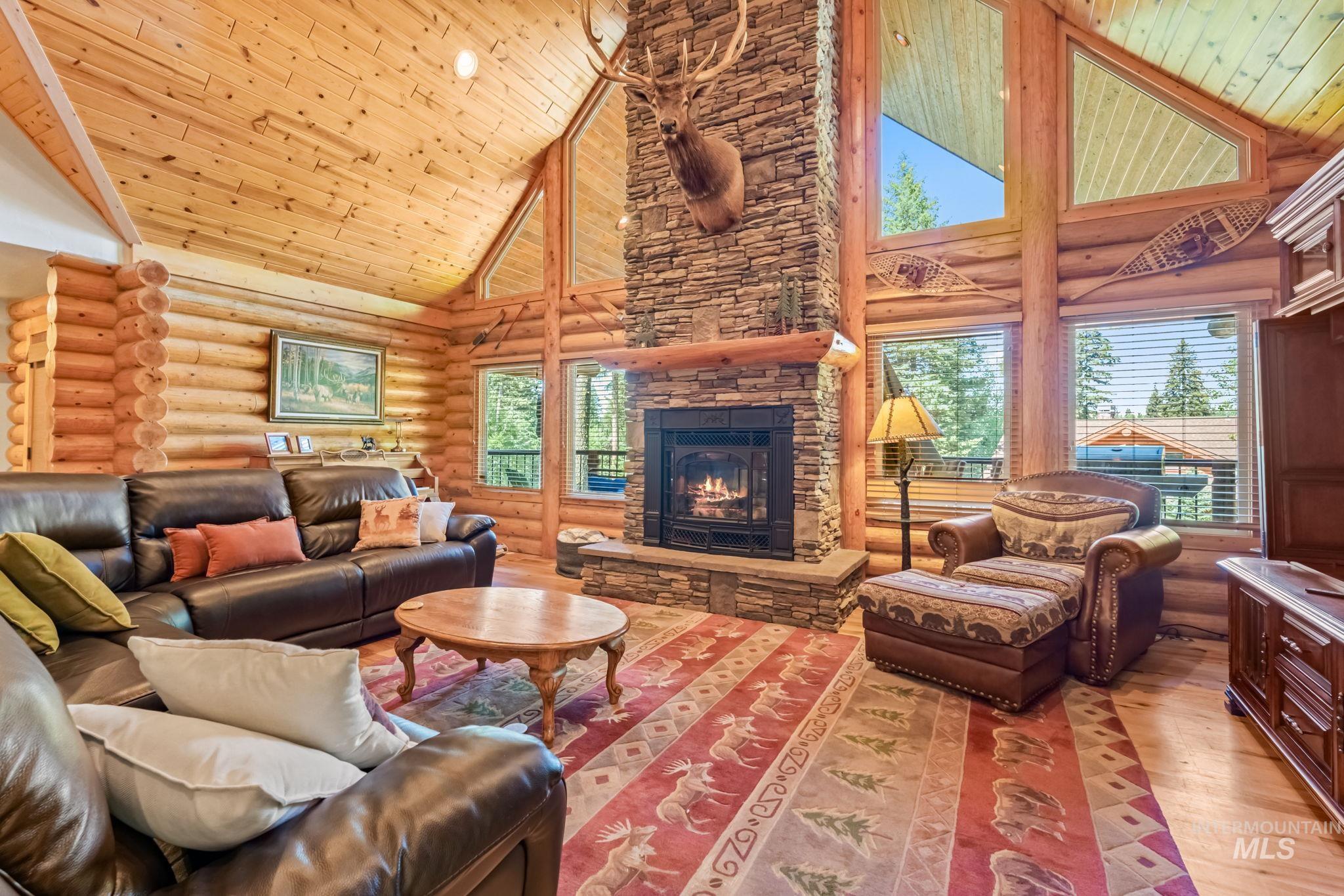 Living room featuring high vaulted ceiling, rustic walls, light wood finished floors, wooden ceiling, and a fireplace