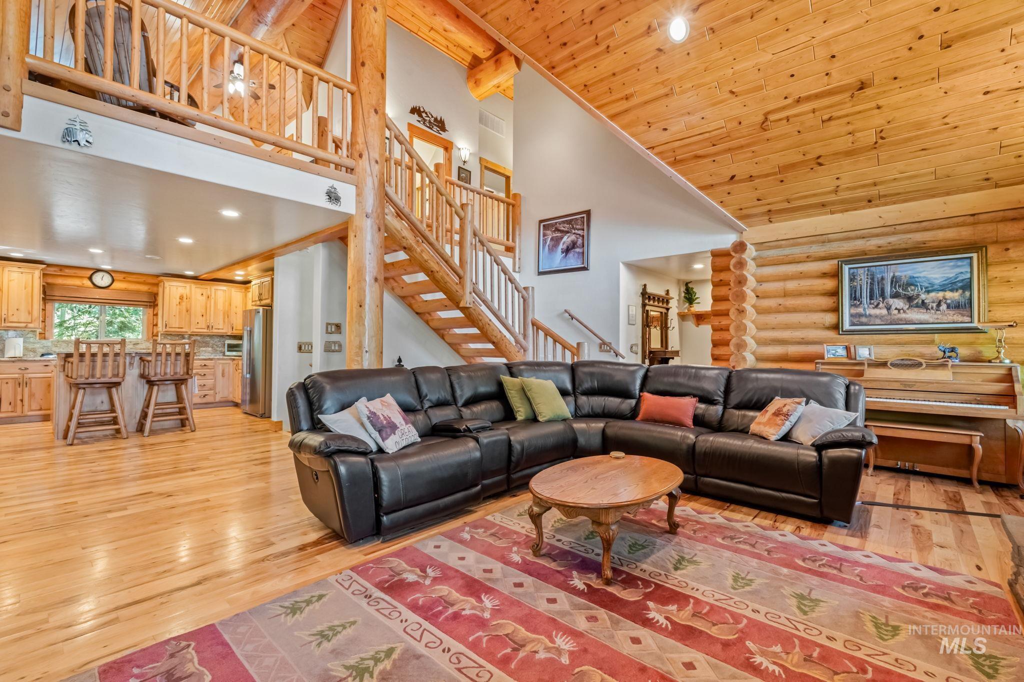 Living room featuring high vaulted ceiling, recessed lighting, stairs, light wood-style floors, and rustic walls