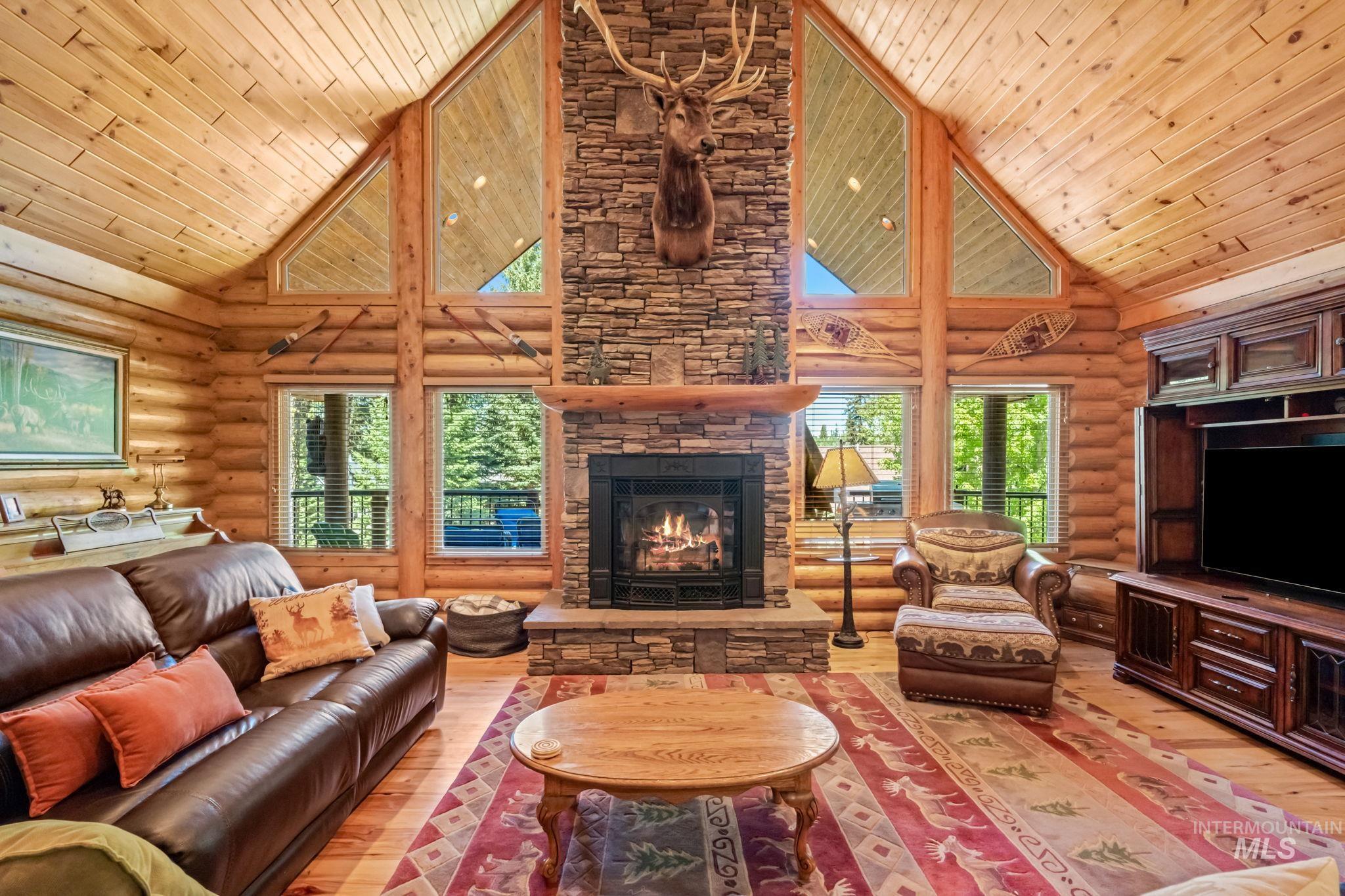 Living room with high vaulted ceiling, light wood-style floors, a fireplace, log walls, and wooden ceiling