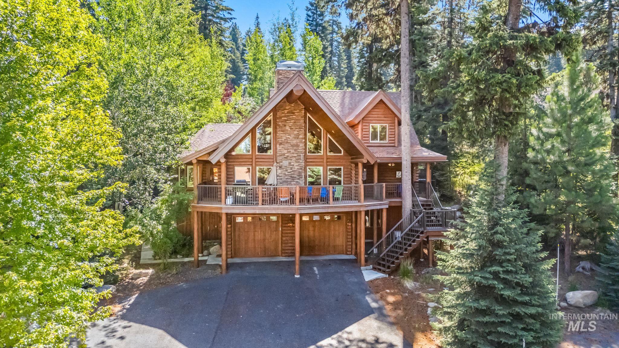 Log-style house featuring a deck, driveway, a chimney, stairway, and an attached garage