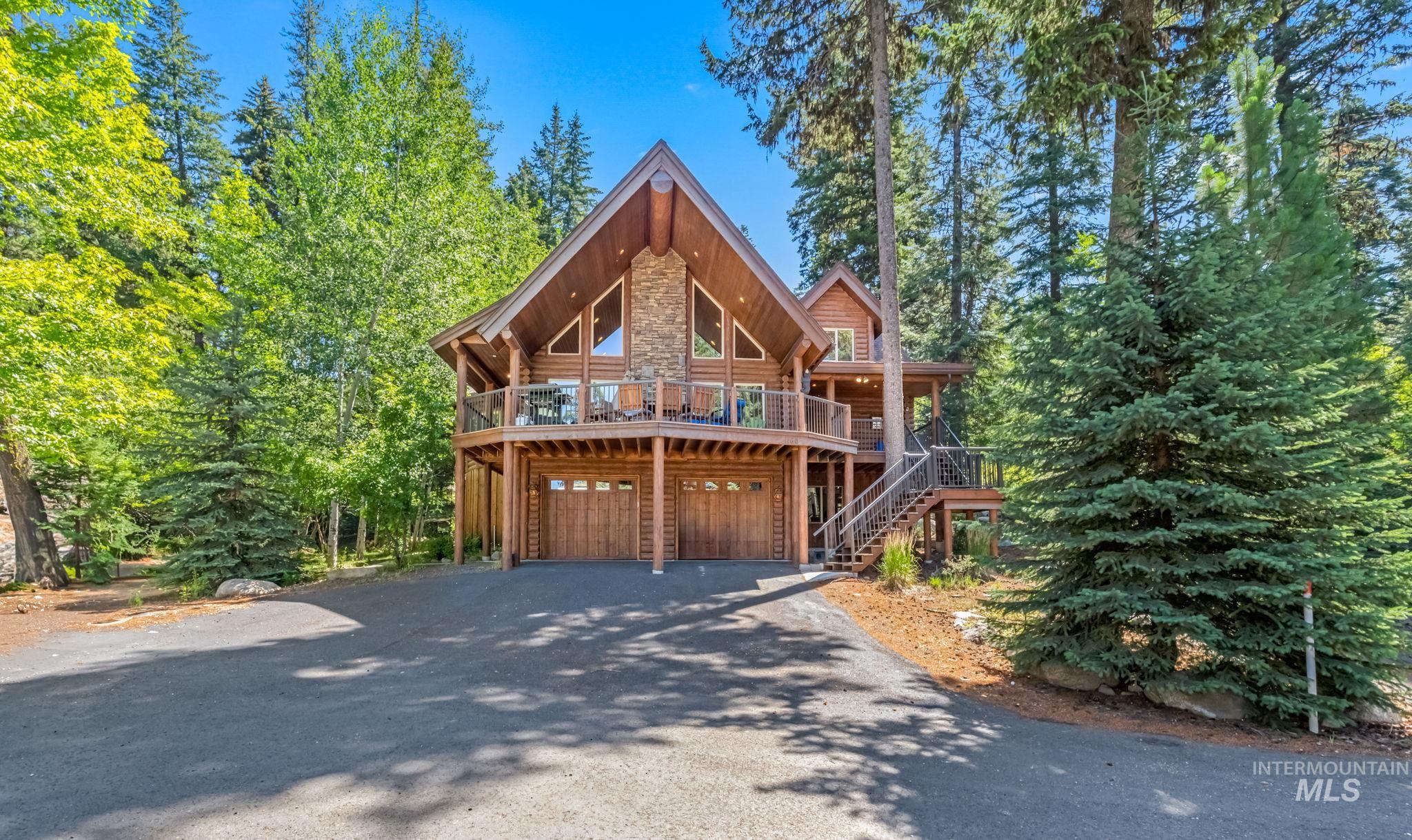 Log cabin featuring a wooden deck, asphalt driveway, stone siding, an attached garage, and stairway