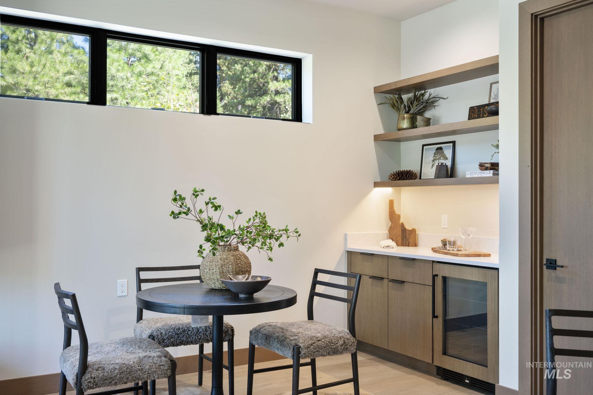 Bar area with light wood-style flooring, wine cooler, modern cabinets, open shelves, and light stone counters