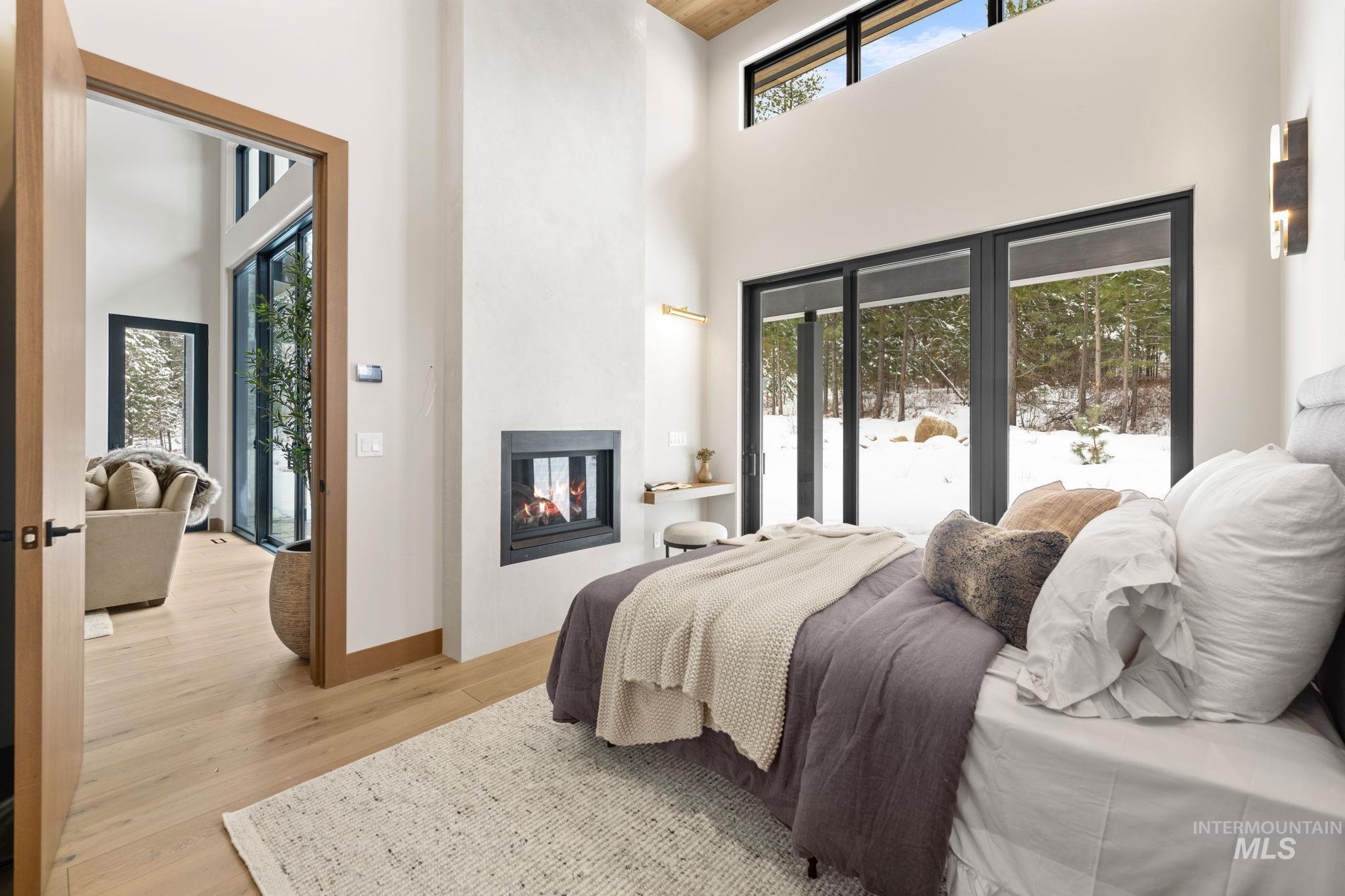 Bedroom featuring access to outside, a towering ceiling, a multi sided fireplace, and light wood-type flooring