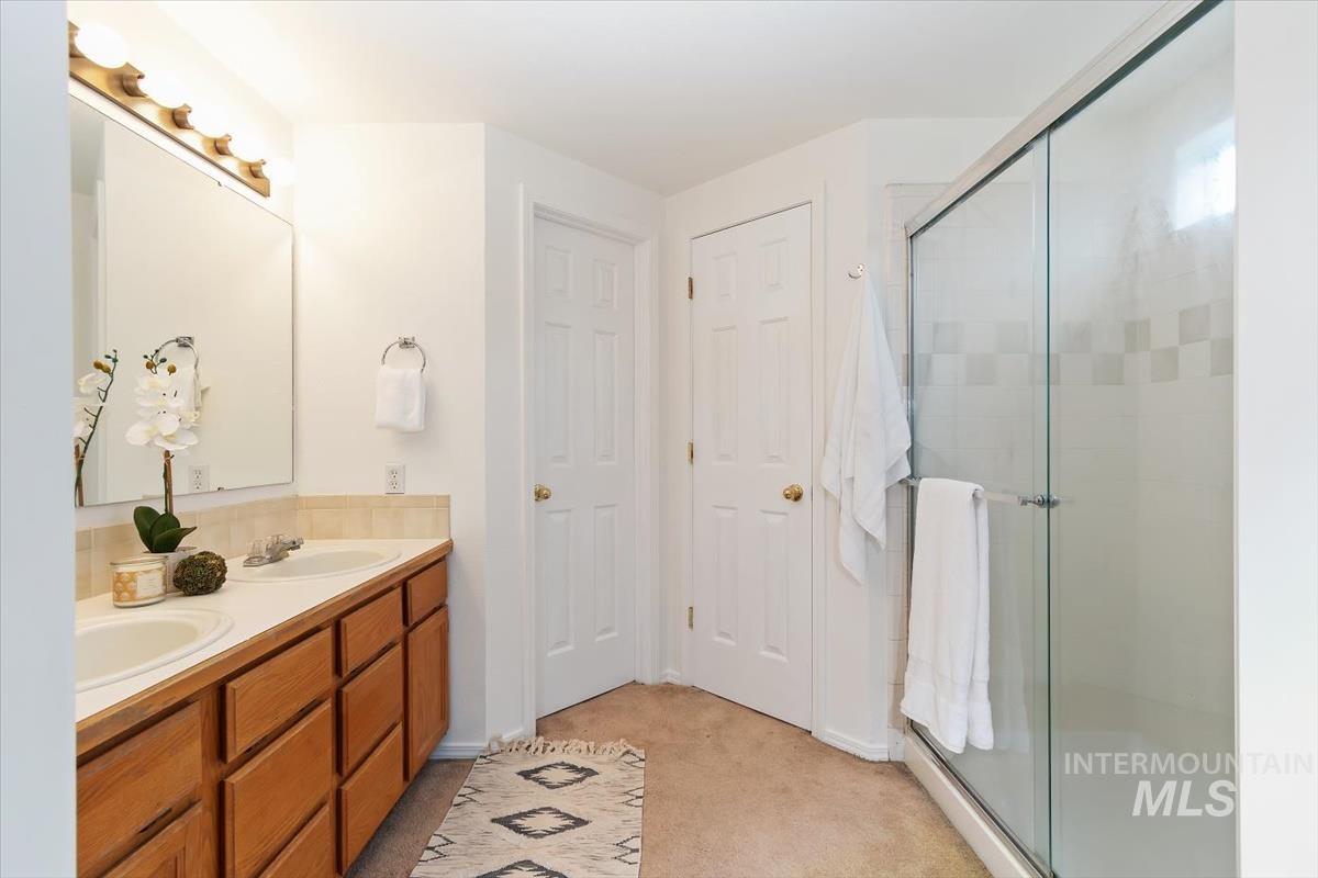 Full bathroom featuring double vanity, light carpet, a stall shower, and baseboard heating