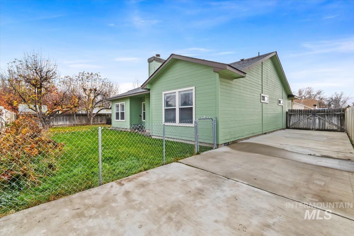 View of side of home with driveway, a chimney, and a gate