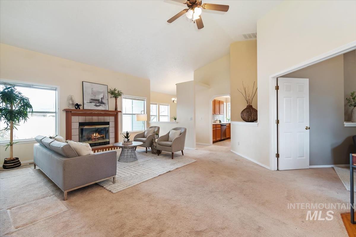 Living area featuring light colored carpet, a tiled fireplace, lofted ceiling, a ceiling fan, and arched walkways