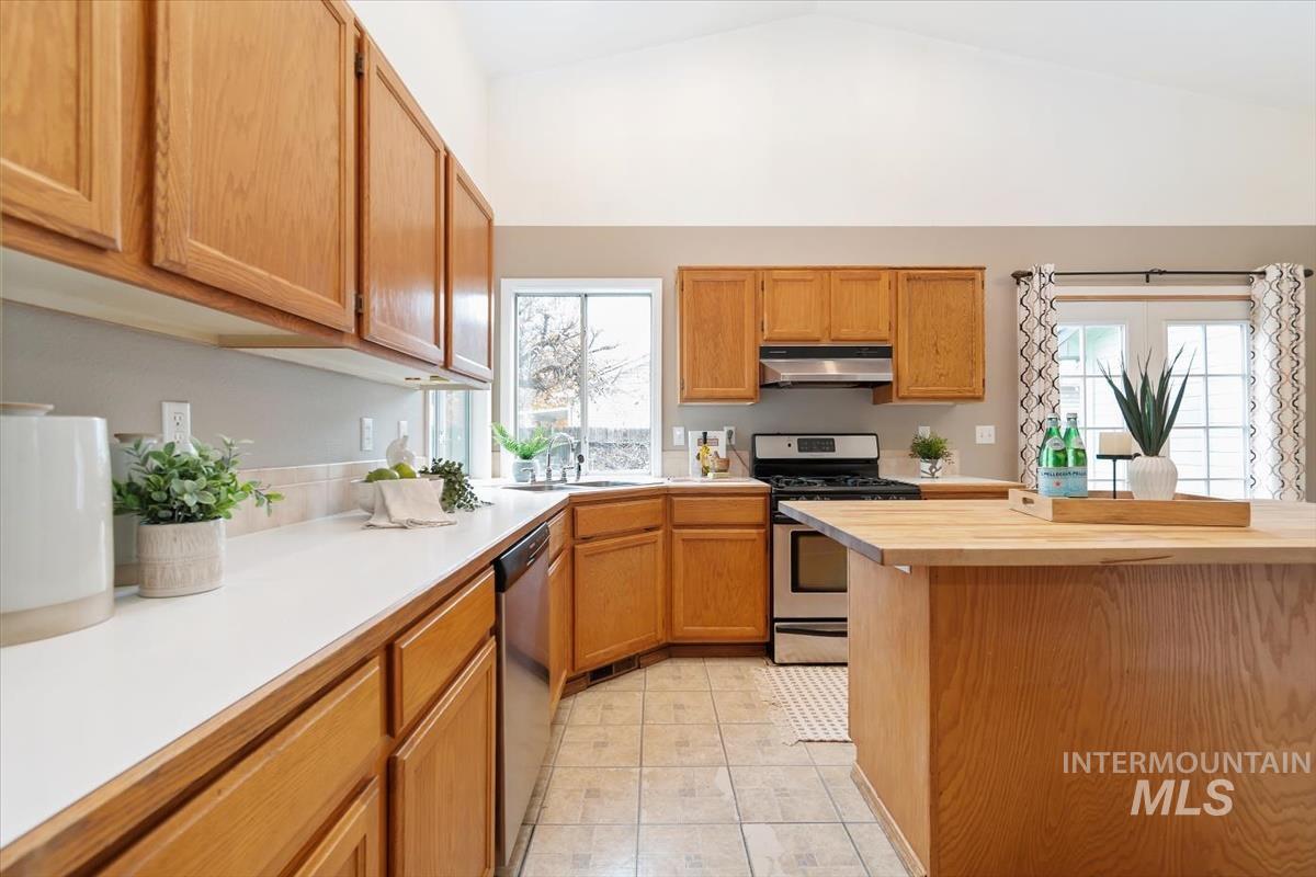 Kitchen with stainless steel appliances, under cabinet range hood, vaulted ceiling, brown cabinetry, and light tile patterned floors