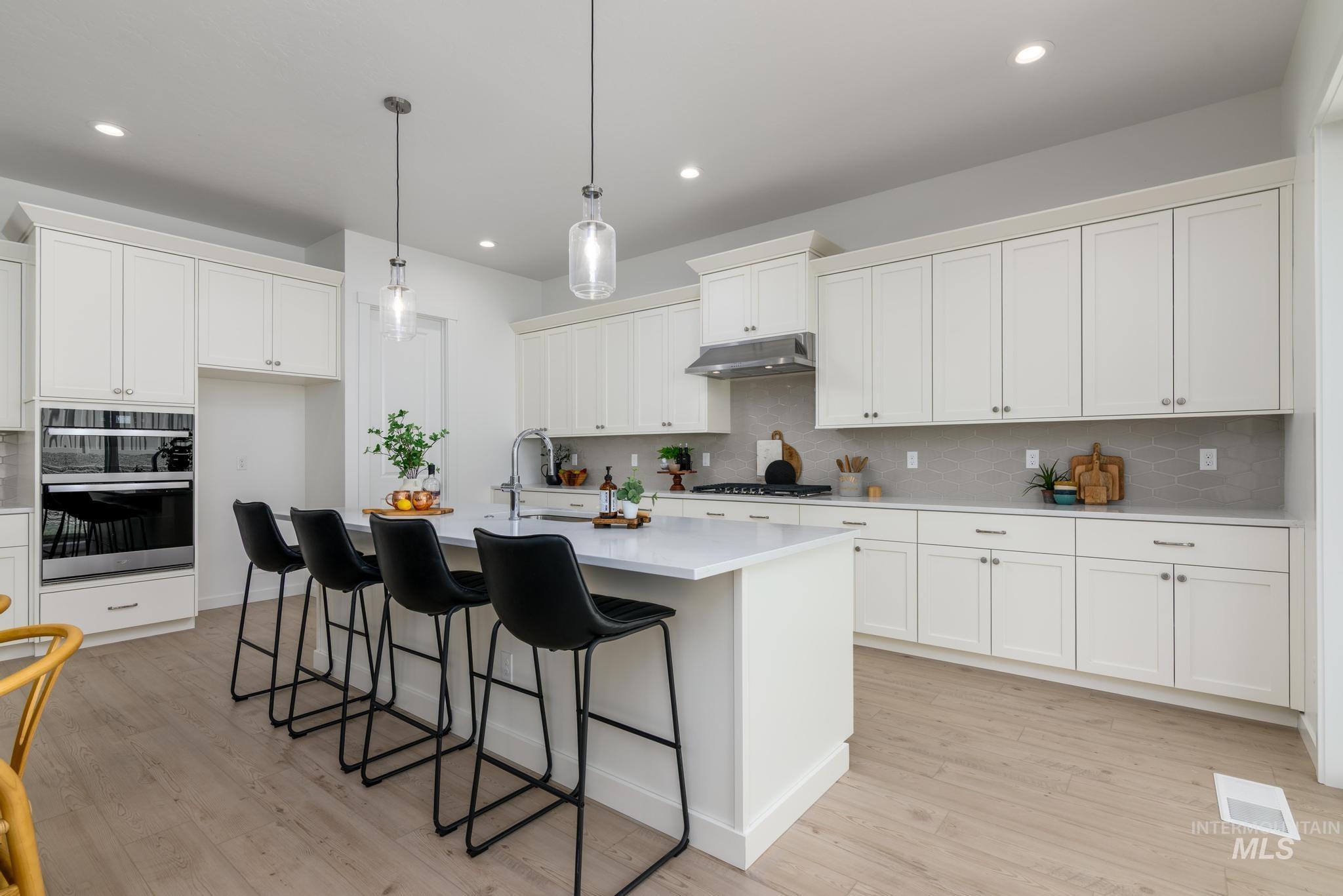 Kitchen featuring decorative backsplash, light countertops, a breakfast bar, a kitchen island with sink, and recessed lighting