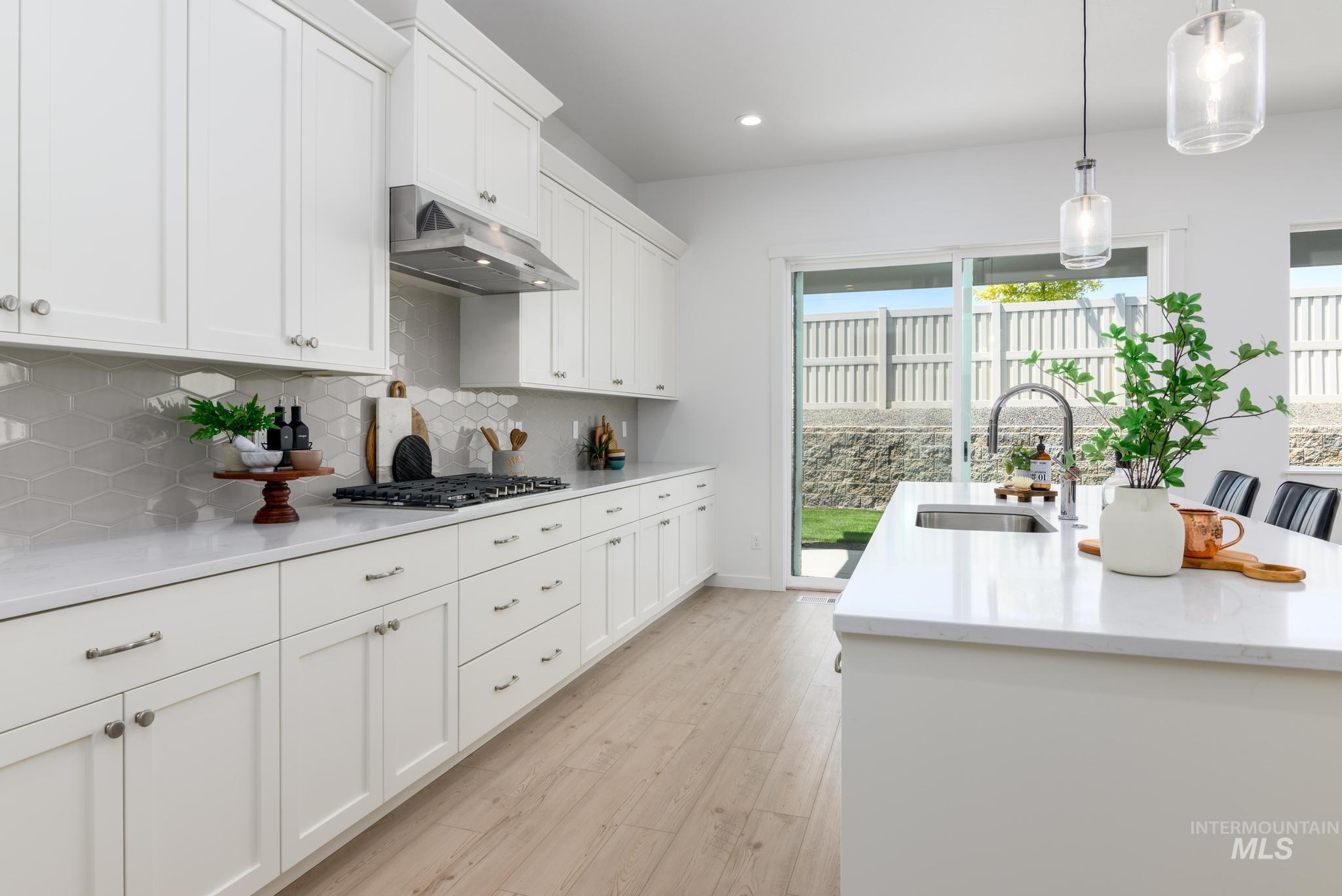 Kitchen with light wood-style floors, white cabinetry, a center island with sink, under cabinet range hood, and recessed lighting