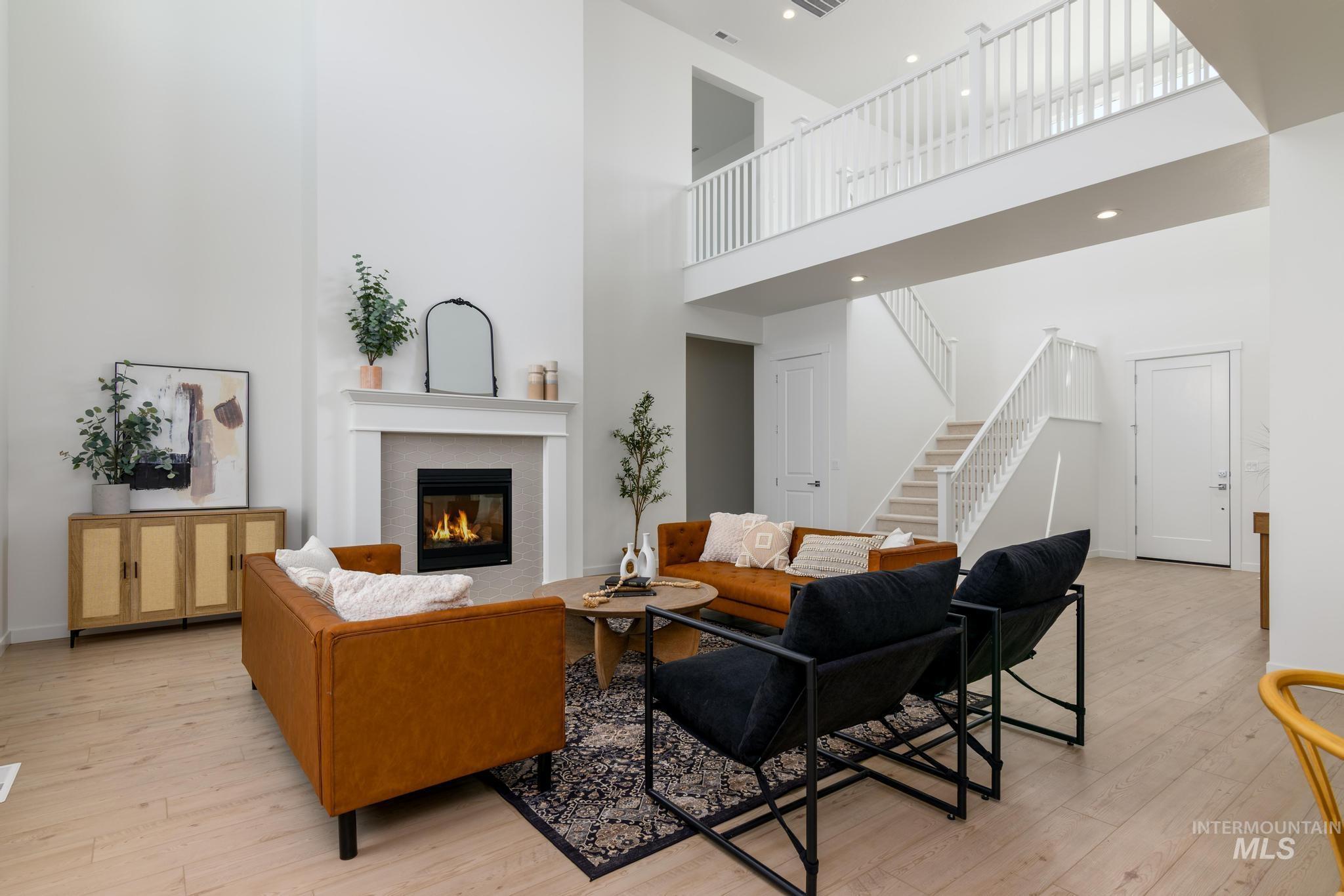 Living area featuring a towering ceiling, a glass covered fireplace, stairway, light wood finished floors, and recessed lighting