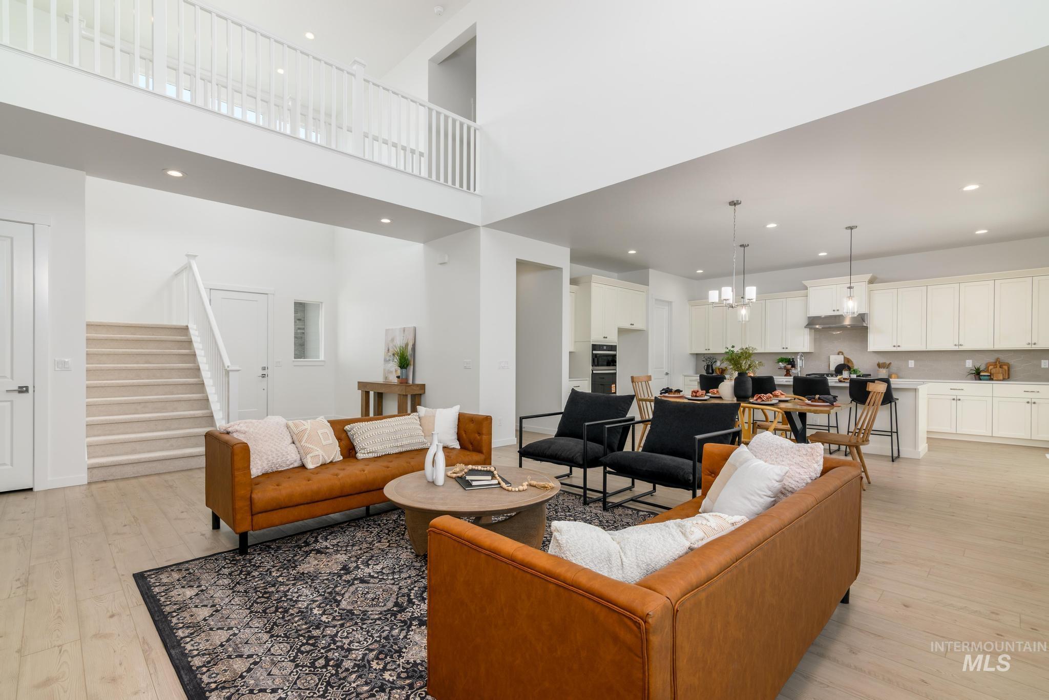 Living room featuring stairs, light wood-style flooring, a chandelier, recessed lighting, and a towering ceiling