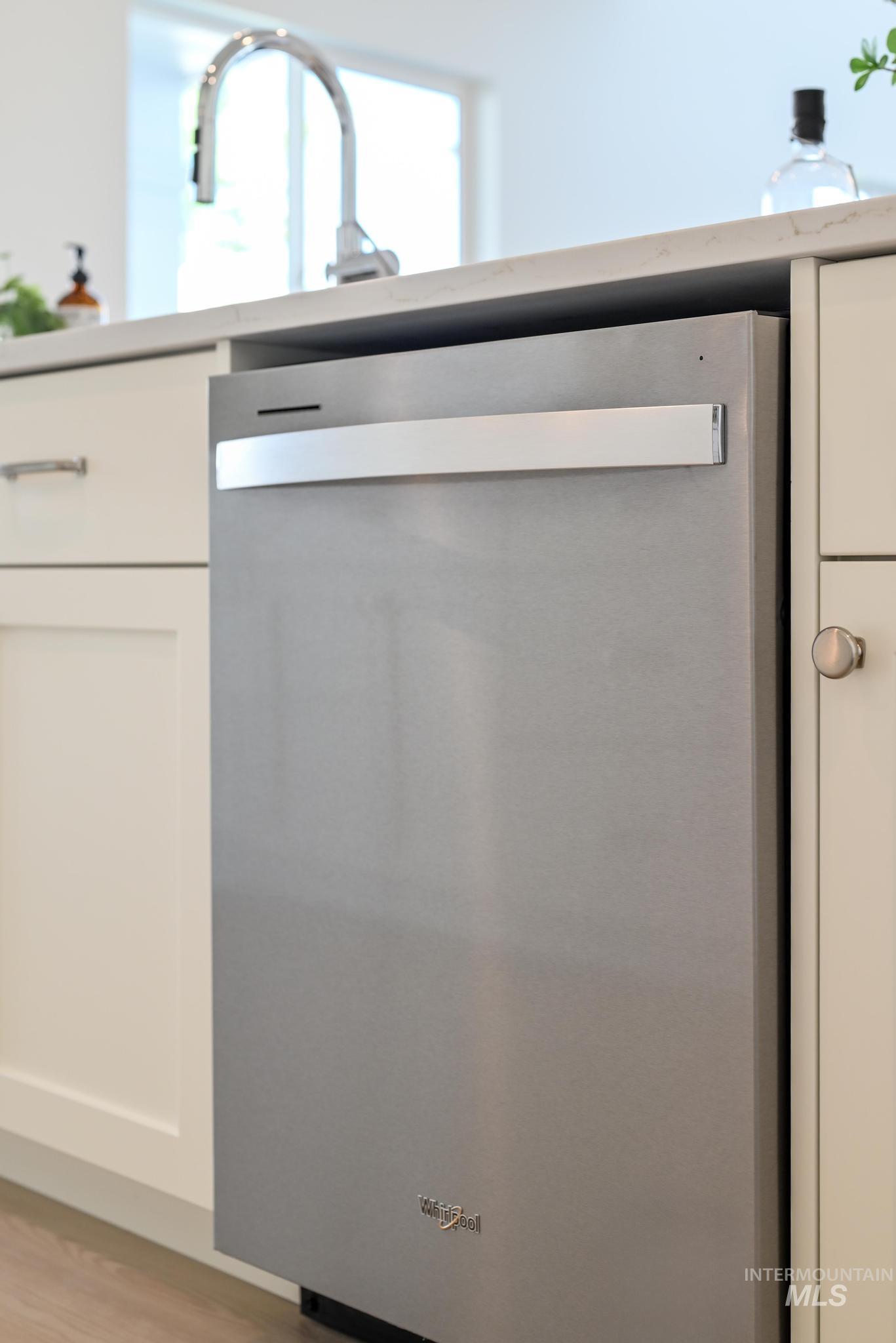 Kitchen view of dishwasher, white cabinetry, light countertops, and light wood-style floors