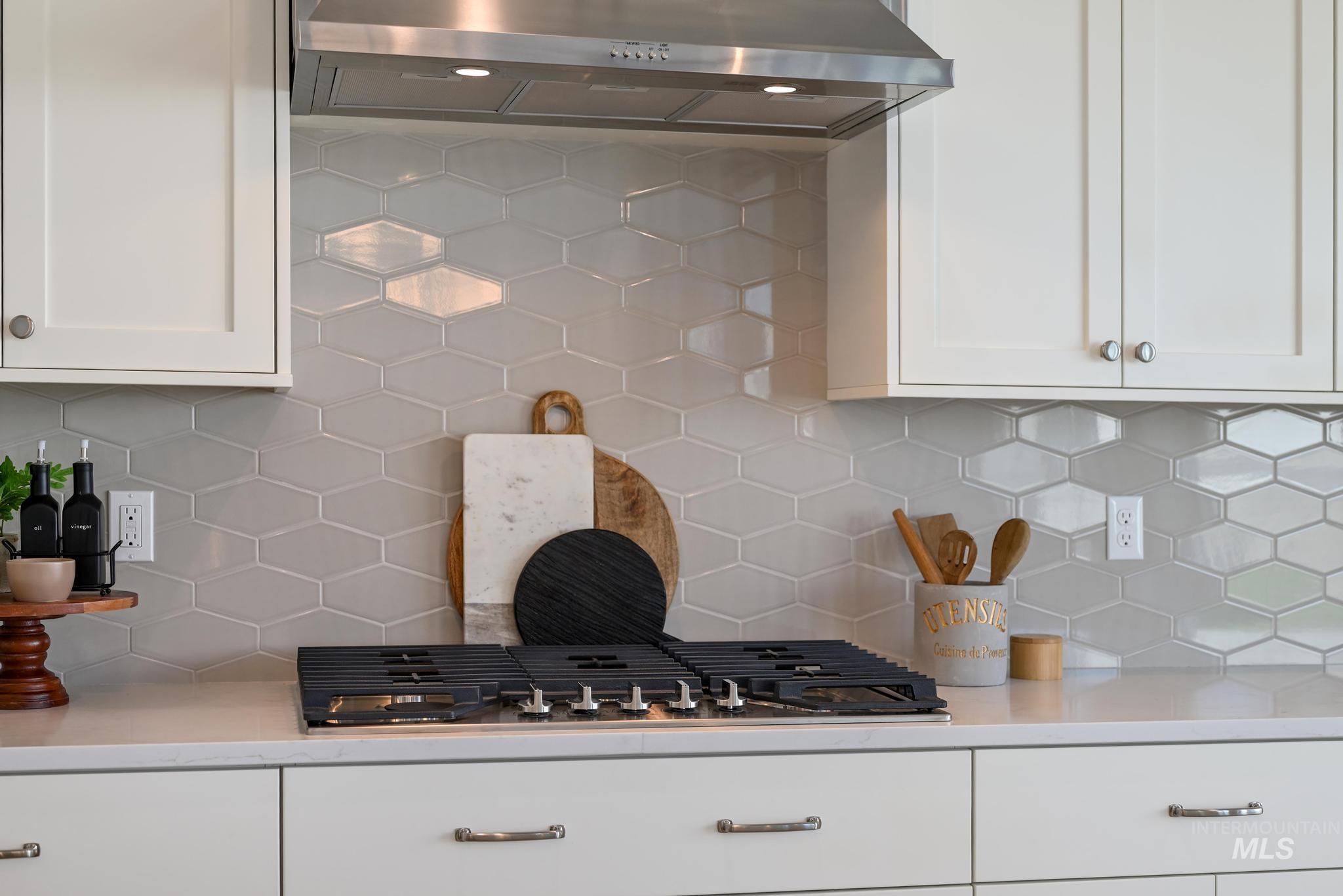 Kitchen with ventilation hood, decorative backsplash, and white cabinetry
