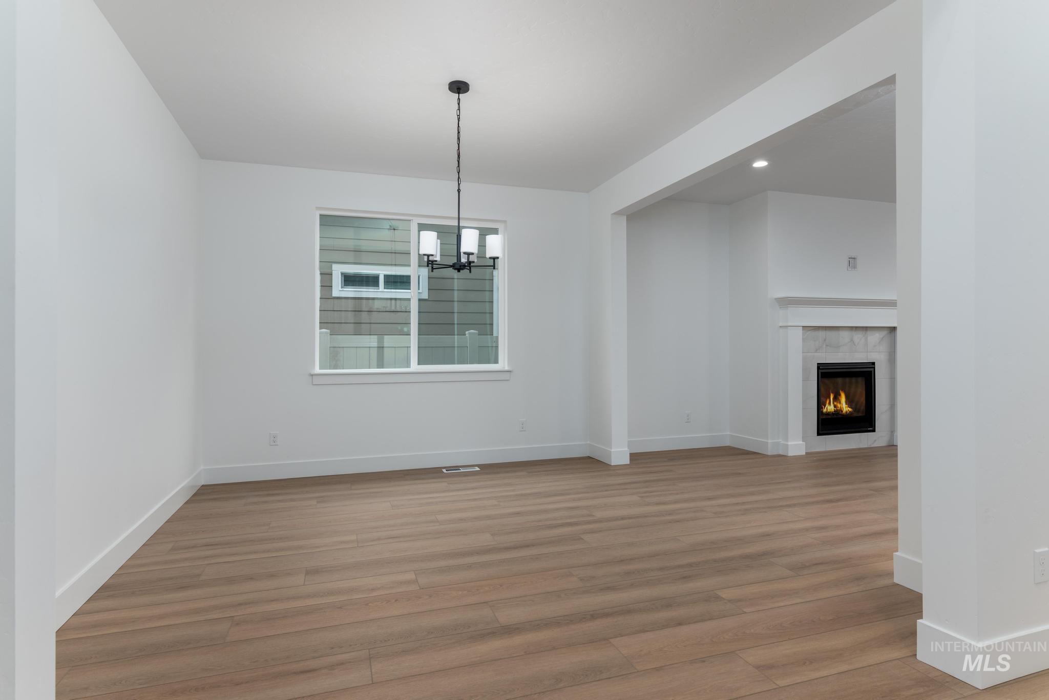 Unfurnished dining area featuring a chandelier, a tiled fireplace, light wood finished floors, and recessed lighting