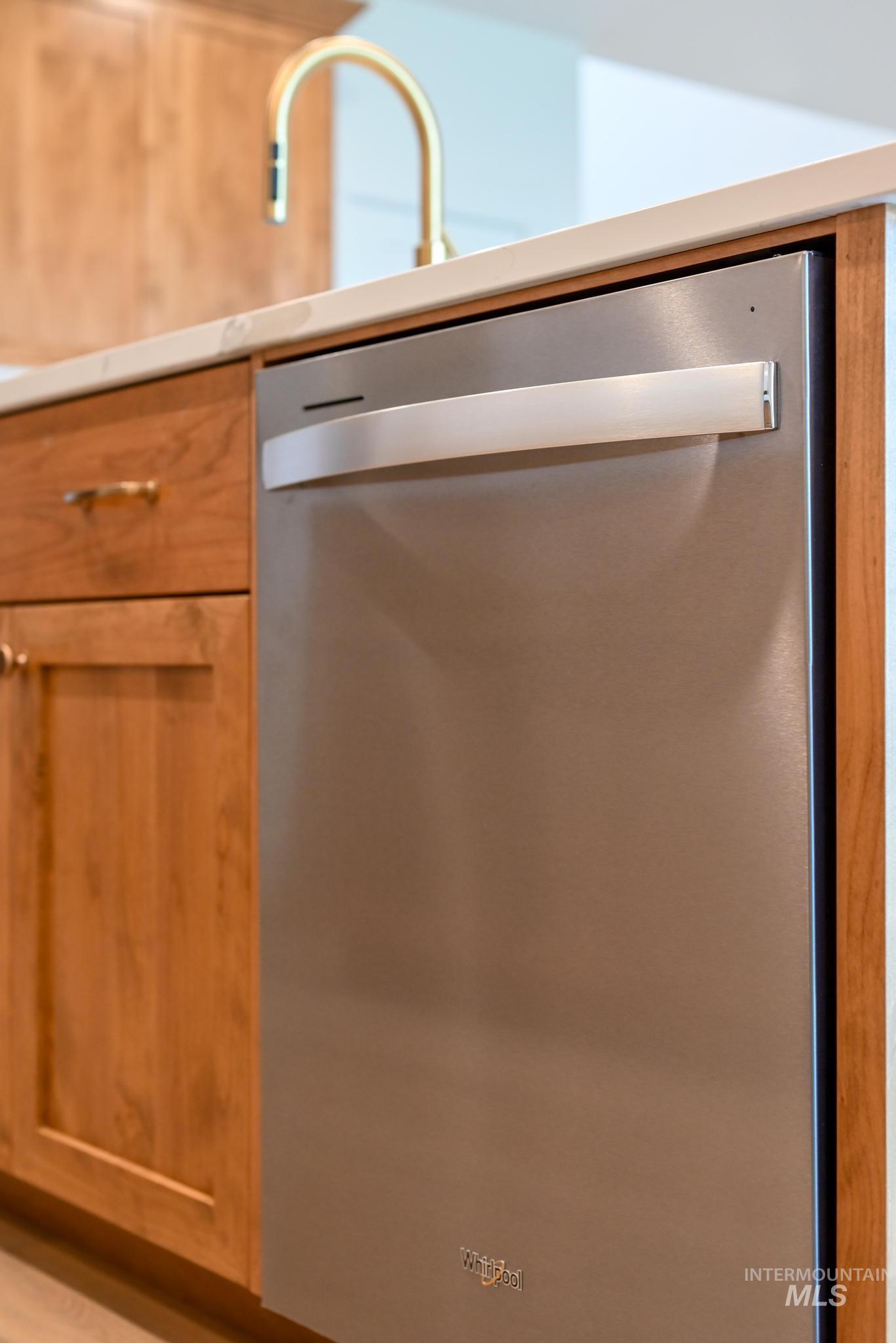 Kitchen view of stainless steel dishwasher, brown cabinetry, and light countertops