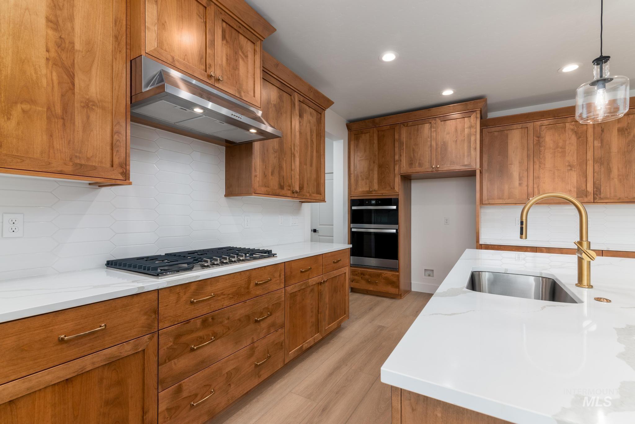 Kitchen with brown cabinets, backsplash, light wood finished floors, recessed lighting, and light stone countertops