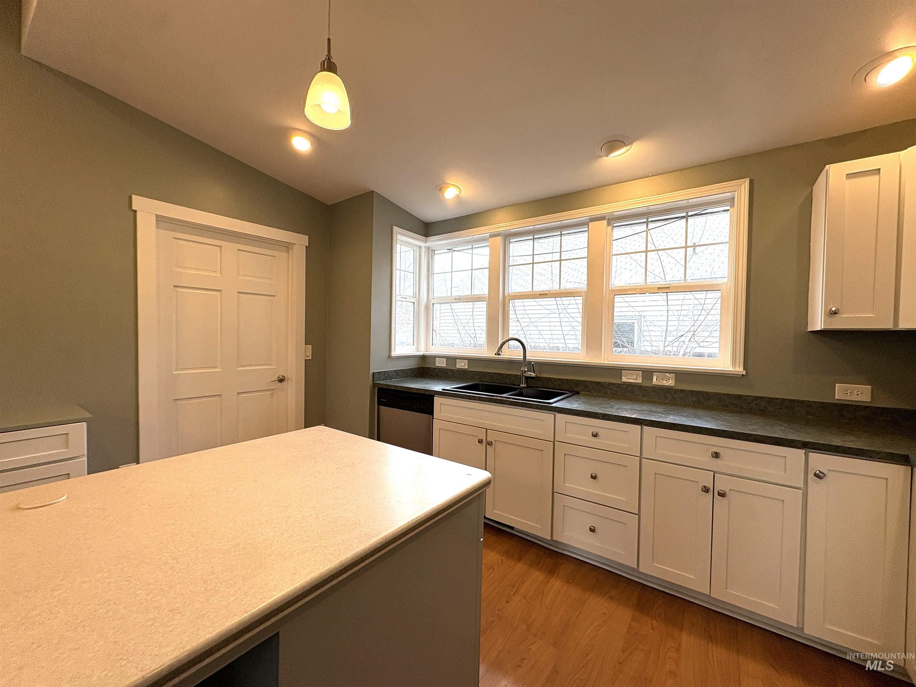 Kitchen featuring pendant lighting,  white cabinets, stainless steel dishwasher, and lofted ceiling