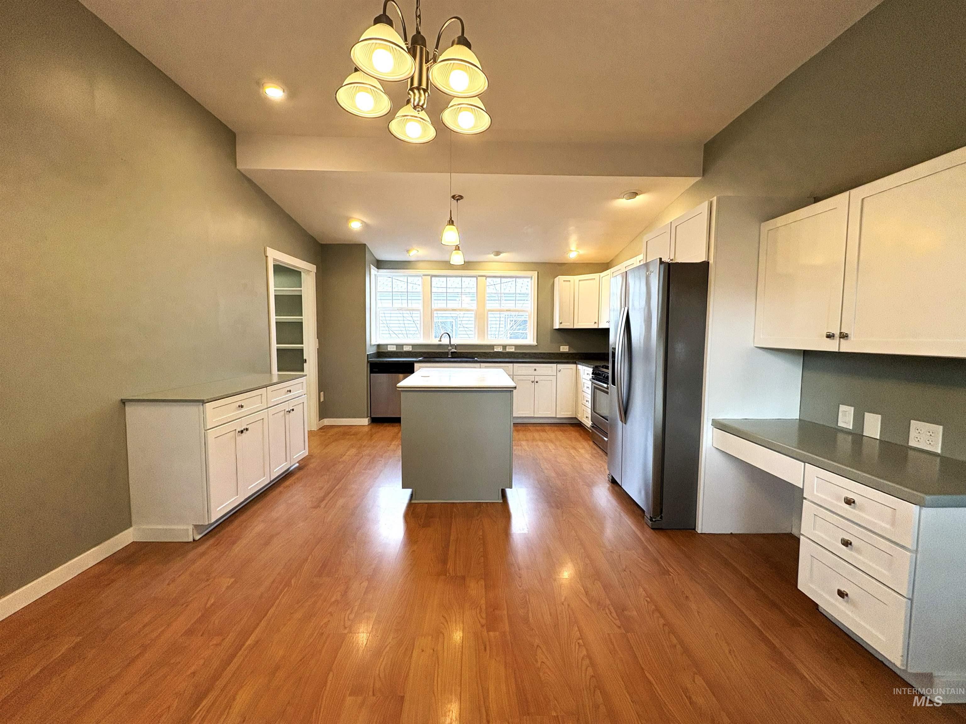 Kitchen featuring dark countertops, stainless steel appliances, white cabinets, dark wood finished floors, and suspended lighting