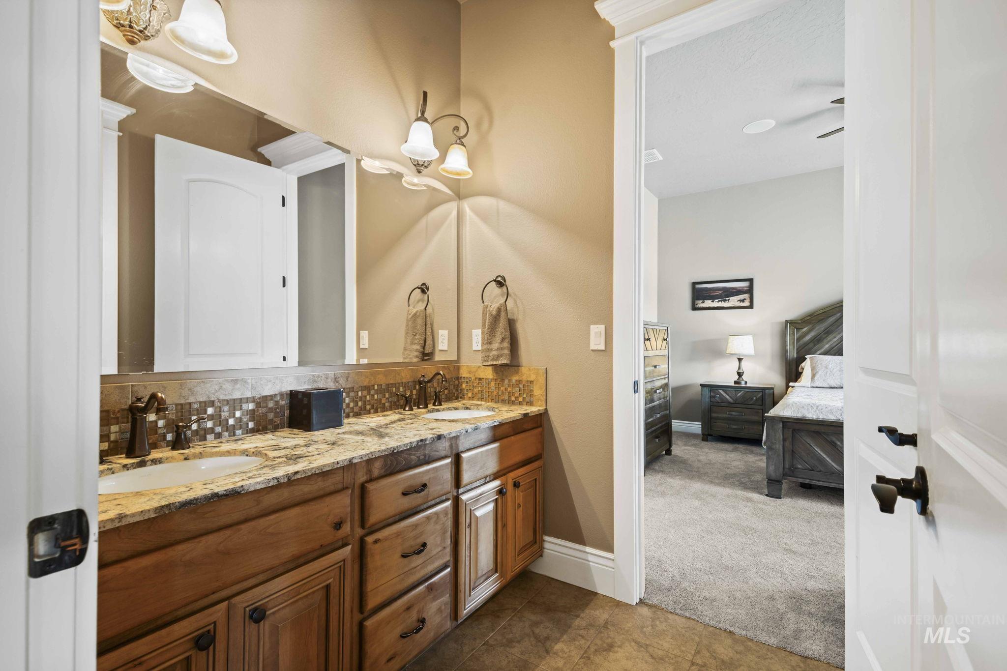 Full bathroom featuring ensuite bath, double vanity, backsplash, and tile patterned flooring