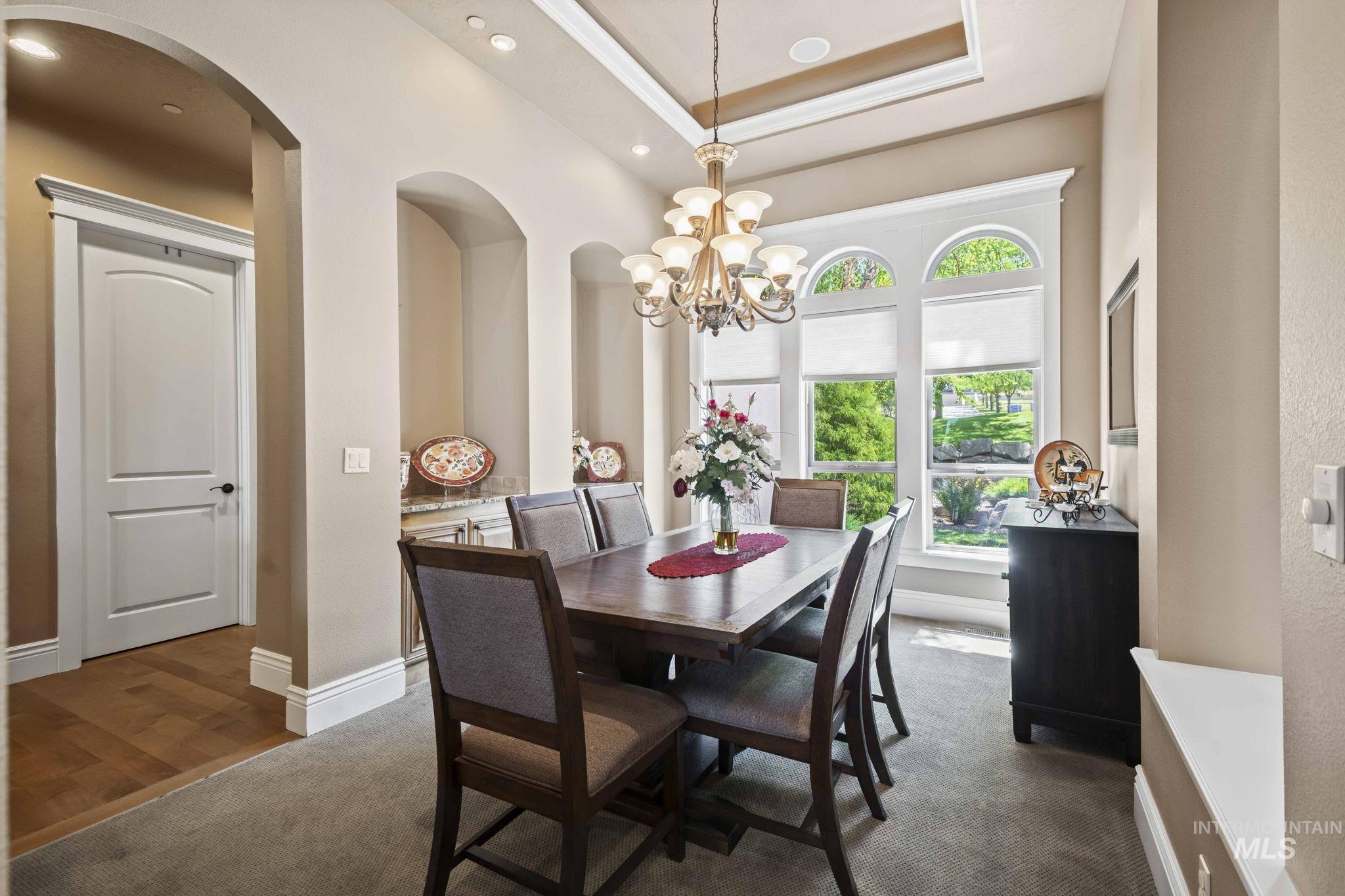 Dining room featuring a chandelier, arched walkways, a raised ceiling, recessed lighting, and dark wood finished floors