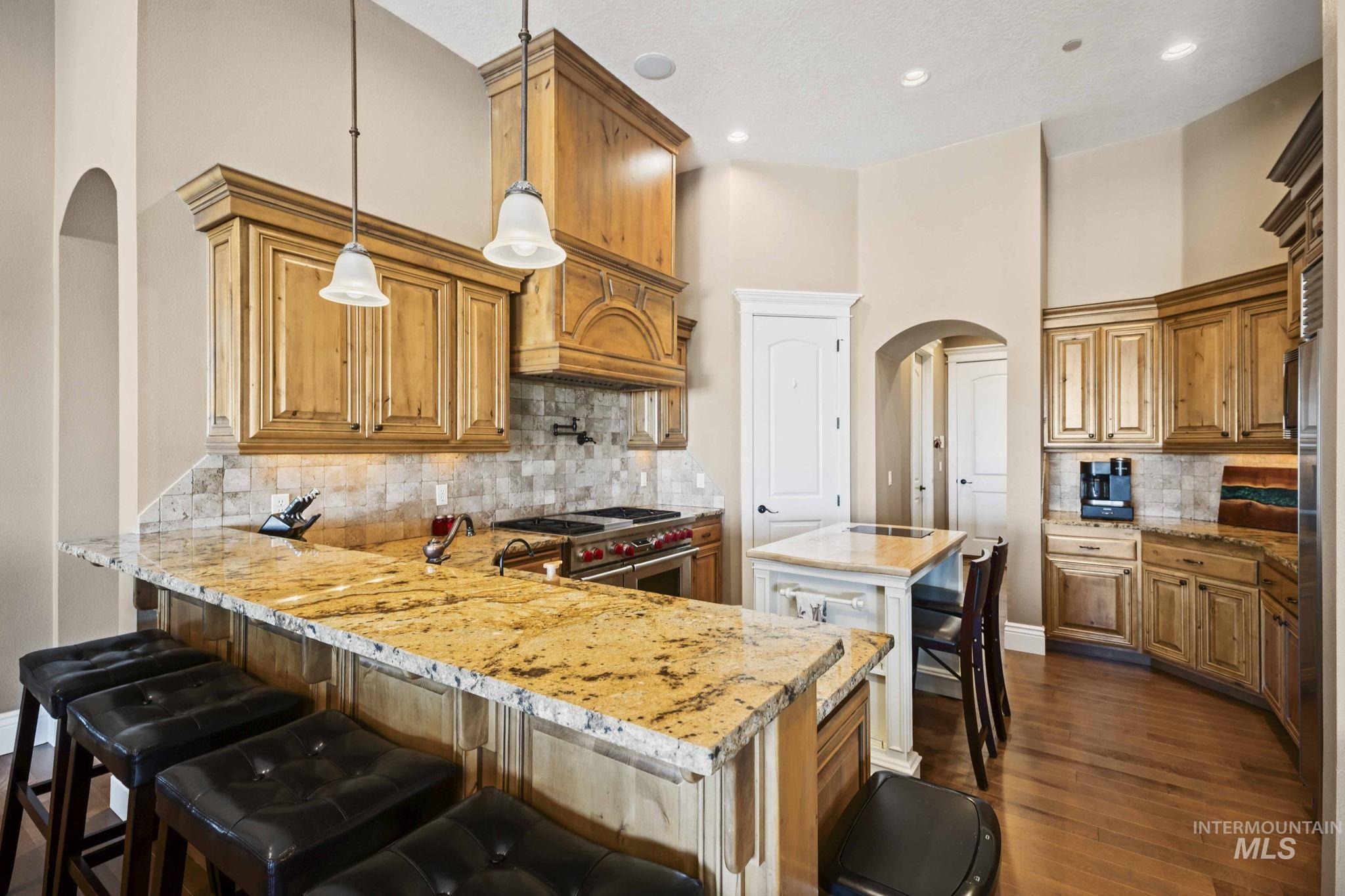 Kitchen featuring arched walkways, tasteful backsplash, a peninsula, dark wood-style flooring, and light stone counters