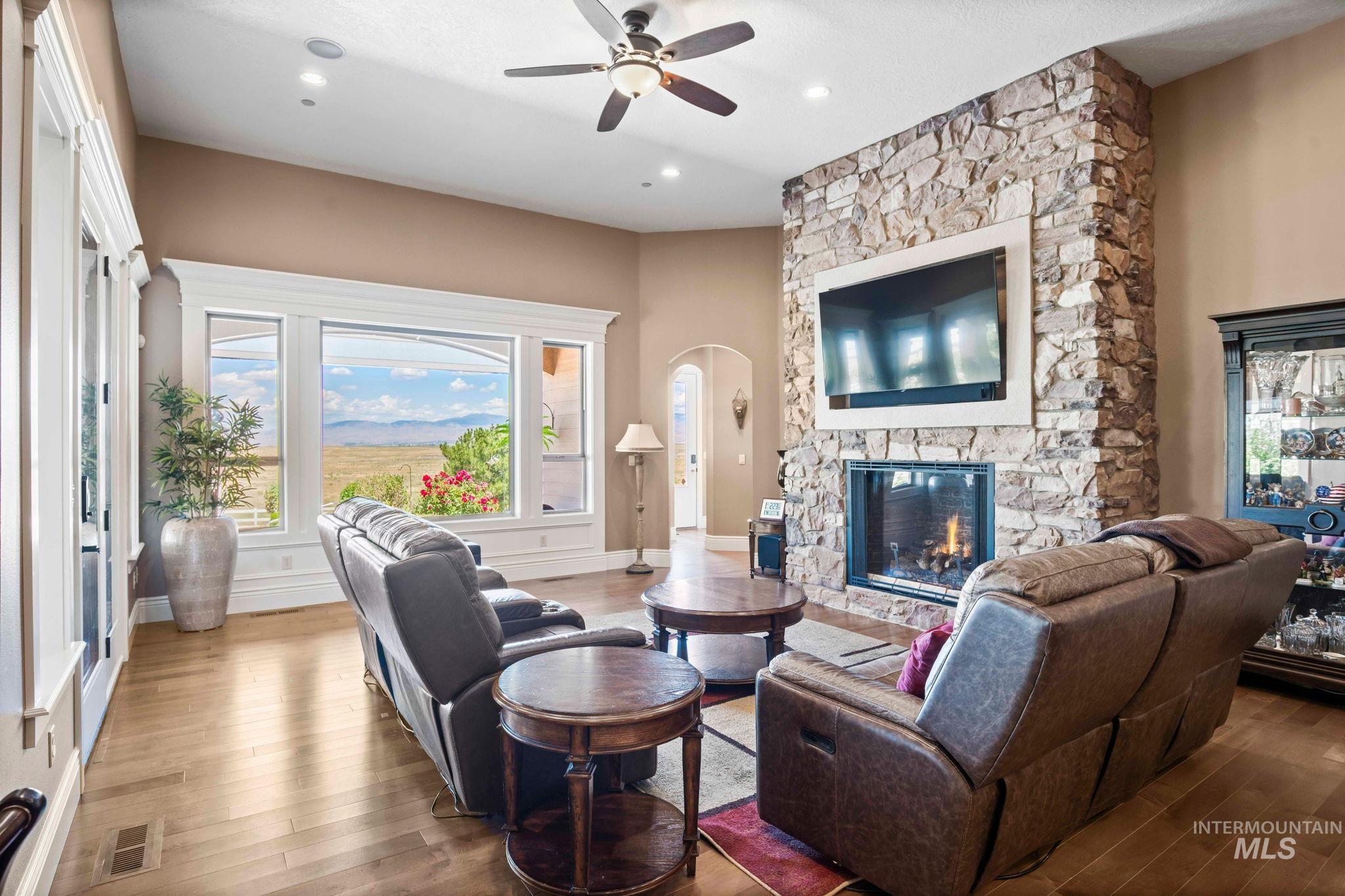Living room with ceiling fan, wood finished floors, a stone fireplace, arched walkways, and recessed lighting