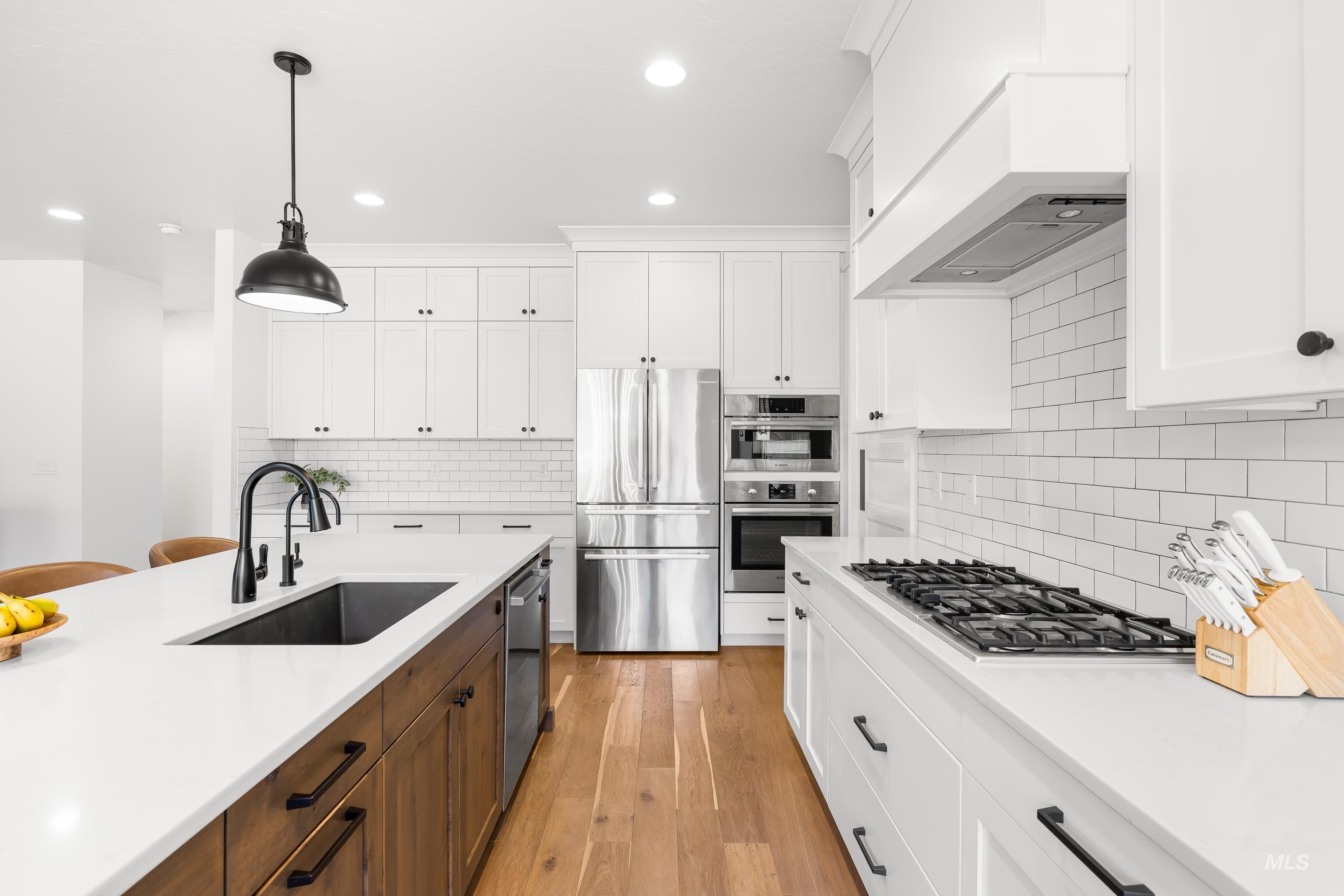 Kitchen featuring appliances with stainless steel finishes, pendant lighting, light wood-type flooring, white cabinets, and recessed lighting