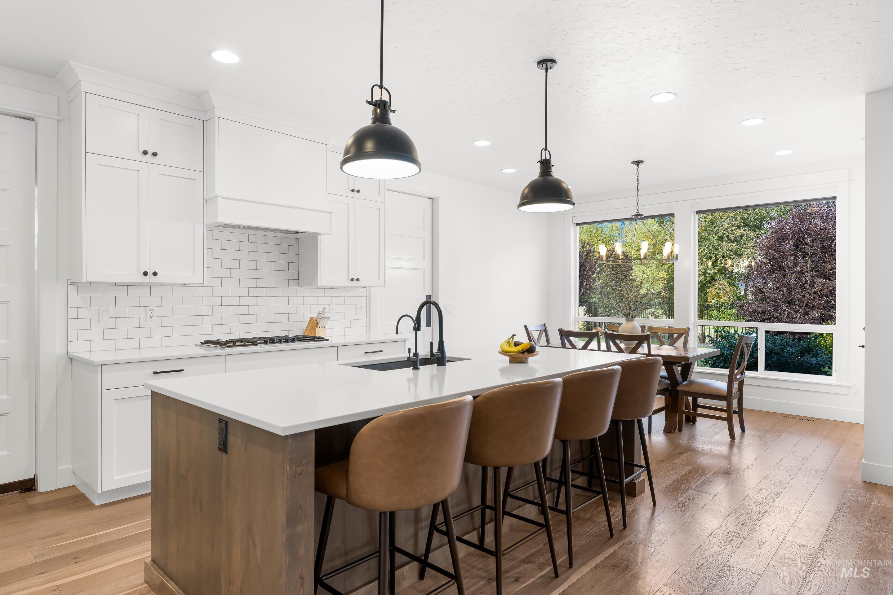 Kitchen with white cabinetry, light wood-type flooring, a center island with sink, hanging light fixtures, and a kitchen bar