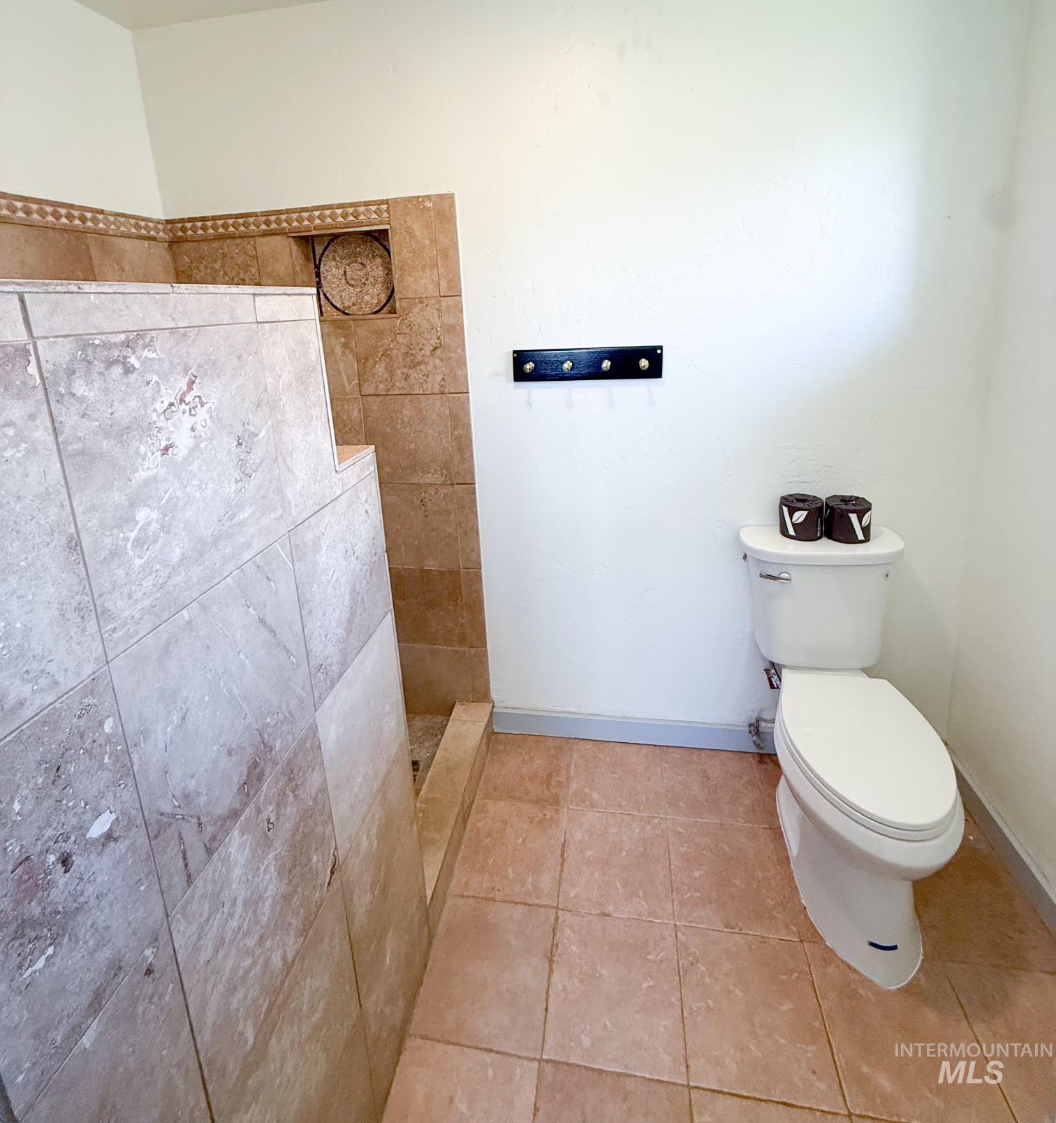 Walk-in shower with natural stone-look tile surround and floor, featuring a built-in niche