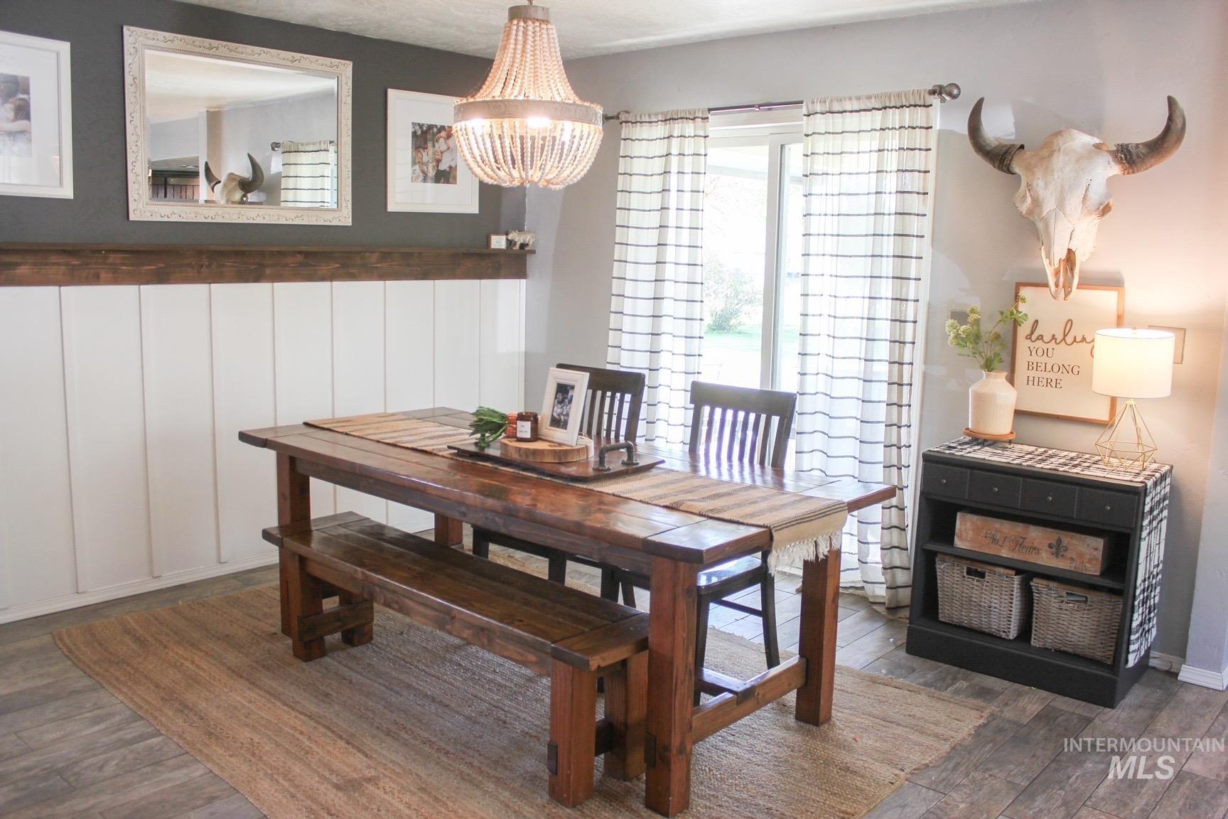 Dining area featuring wood-finish flooring, white wainscoting with a dark wood cap, and a beaded chandelier