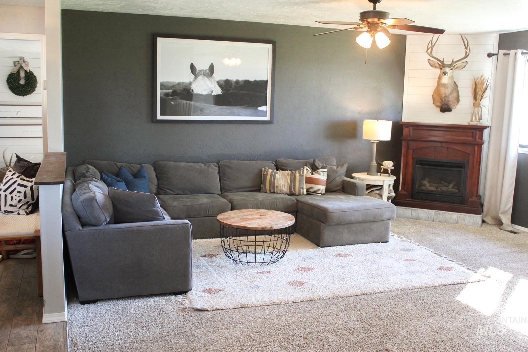 Living area featuring a corner fireplace with a rich wood mantel, a ceiling fan with integrated lighting, and carpet flooring
