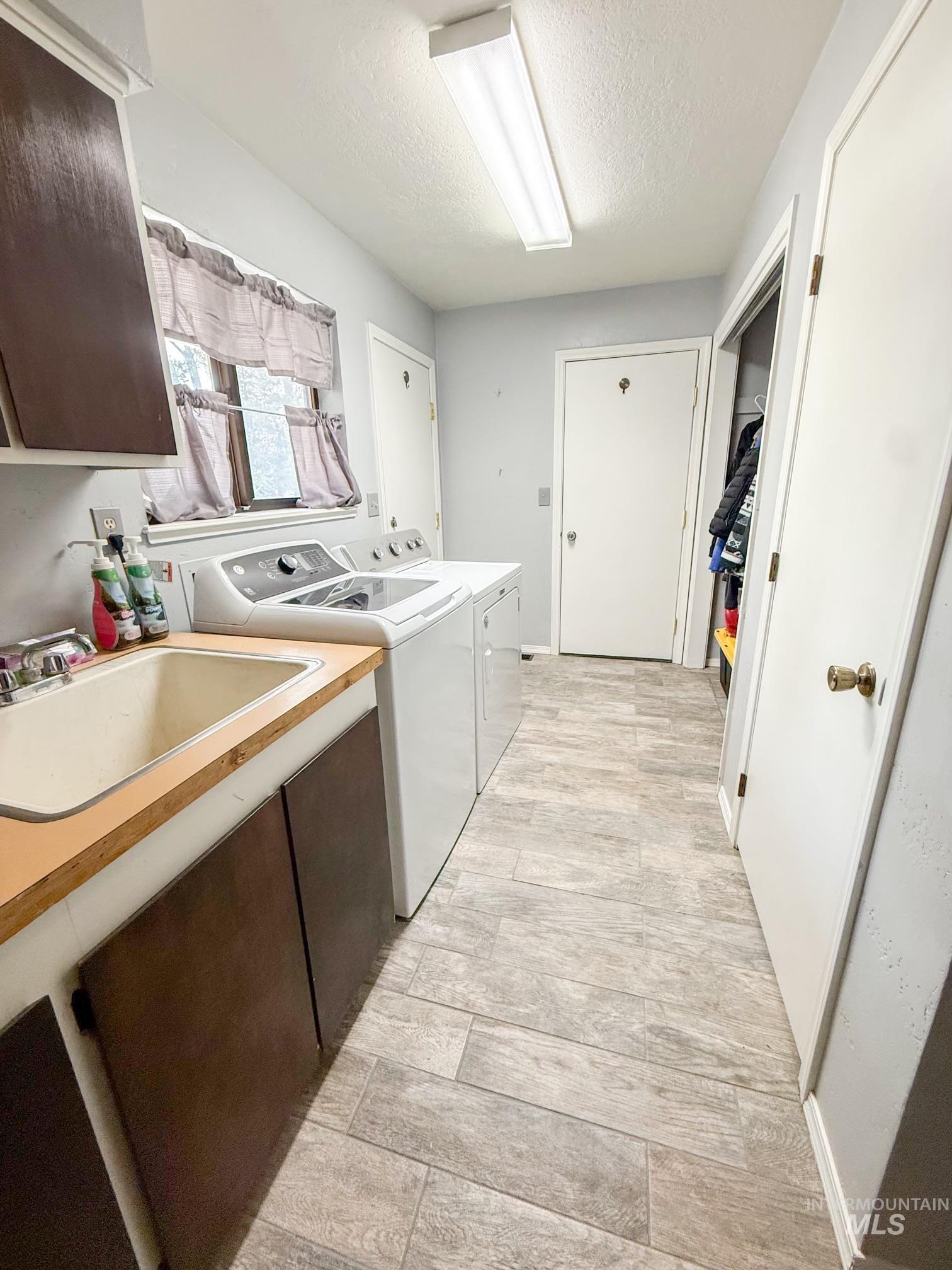 Dedicated laundry area featuring wood-finish flooring, a utility sink with a wood countertop, and ample storage cabinetry