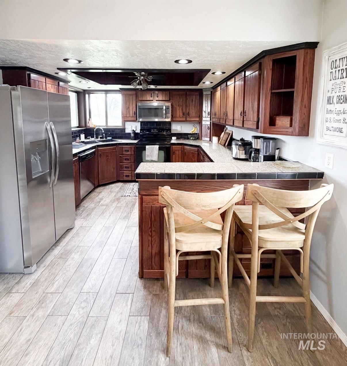 U-shaped kitchen featuring wood-finish cabinetry, stainless steel appliances, and a tiled countertop