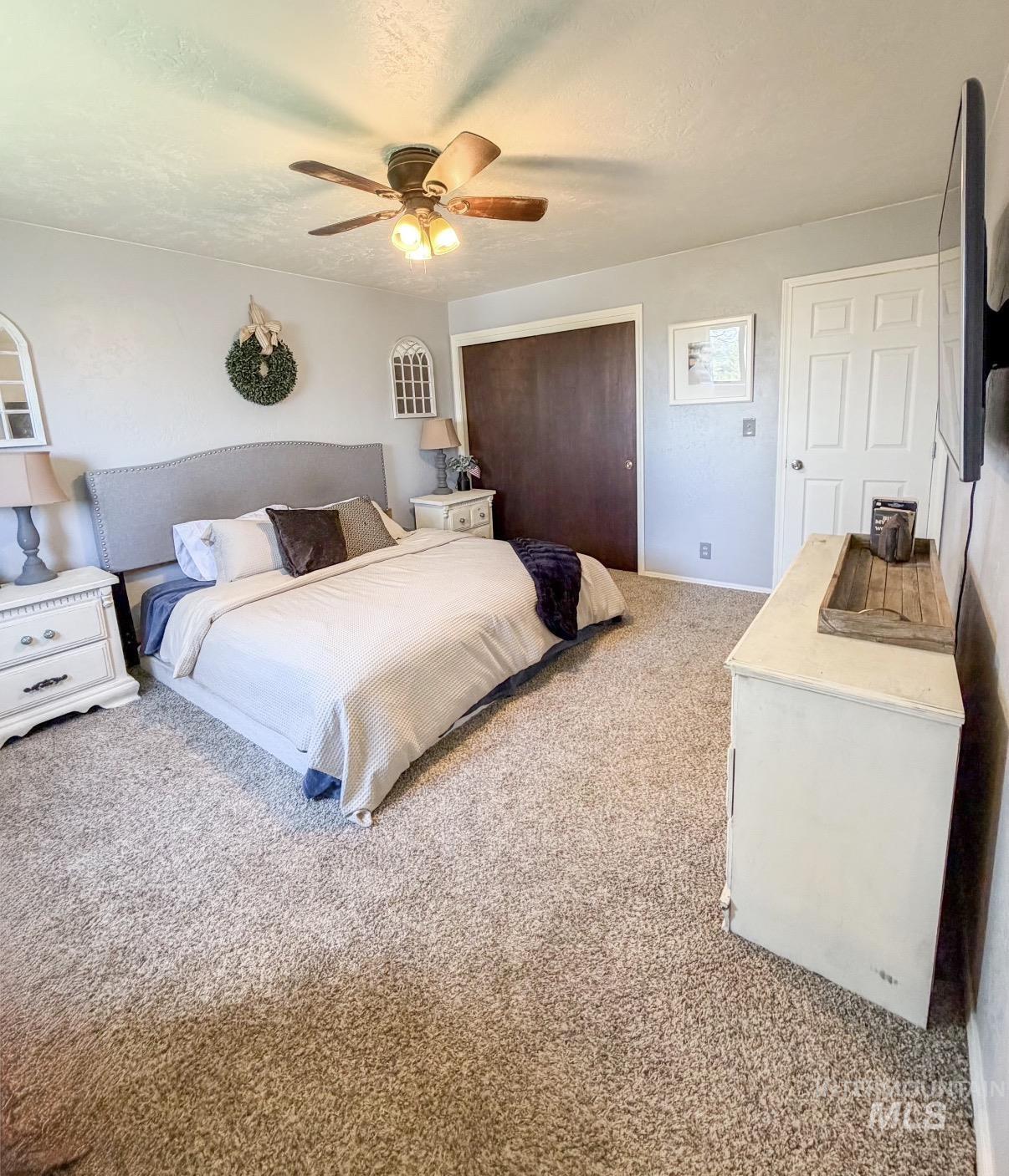 Spacious bedroom featuring neutral carpeting, a ceiling fan with integrated lighting, and light gray painted walls