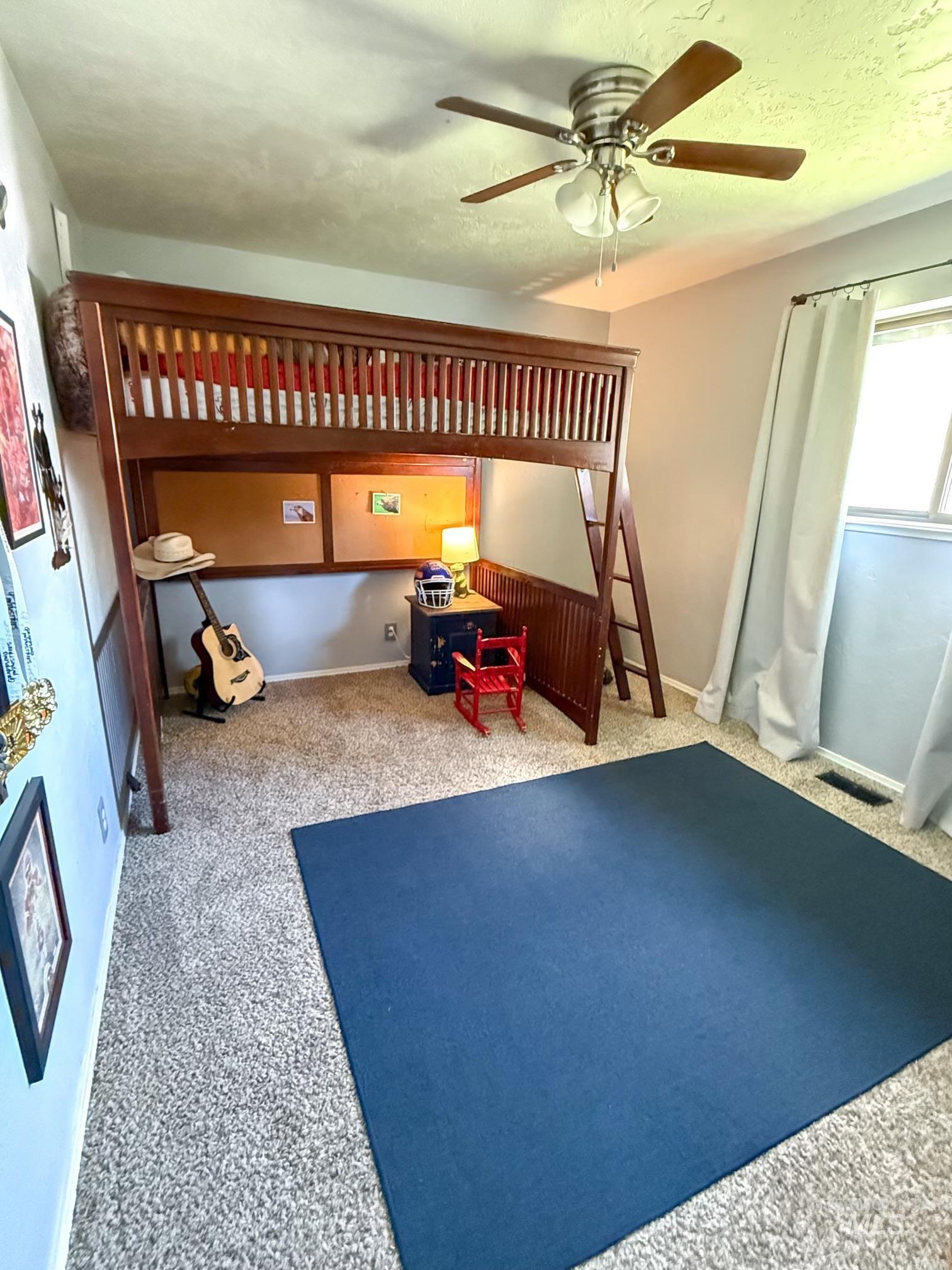 Carpeted room featuring a ceiling fan with light fixture, window with curtains, and light-toned wall paneling