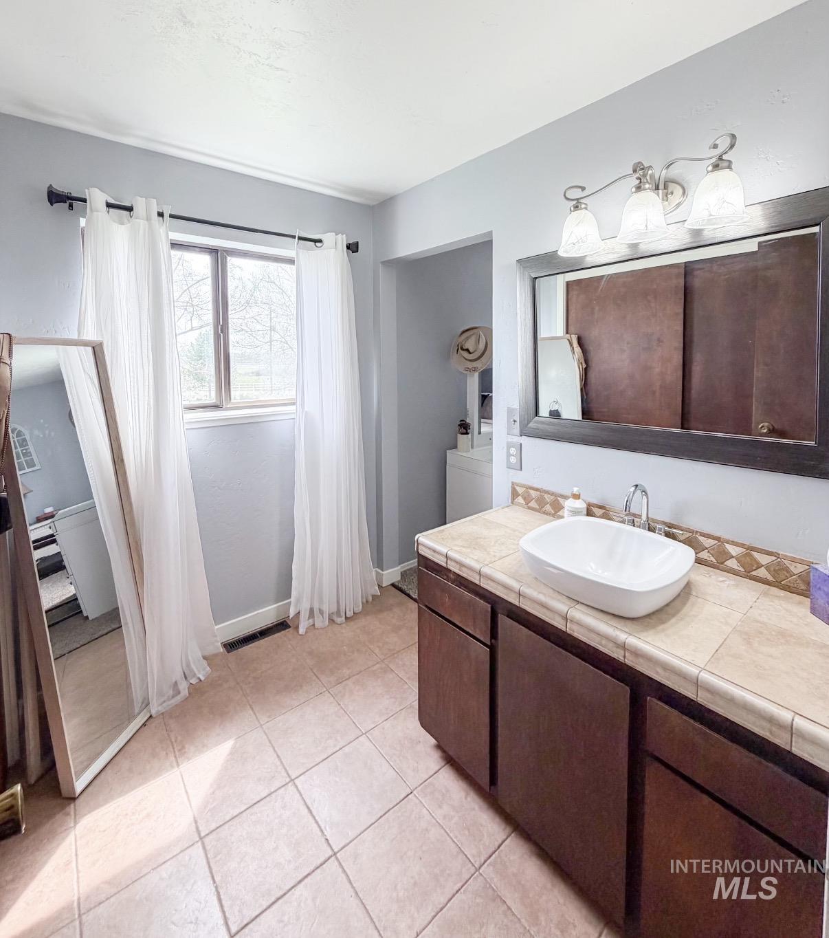 Bathroom vanity featuring a vessel sink, tile countertop, and dark wood cabinetry