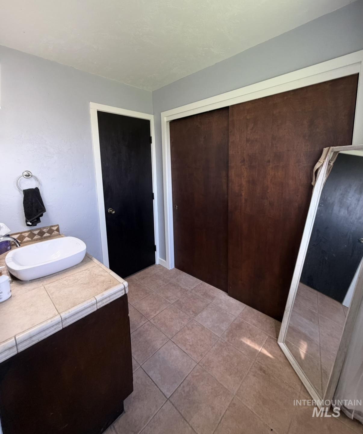 Bathroom featuring a tile-top vanity with vessel sink, wood-finish cabinetry, tile flooring, and dark wood-finish sliding closet doors